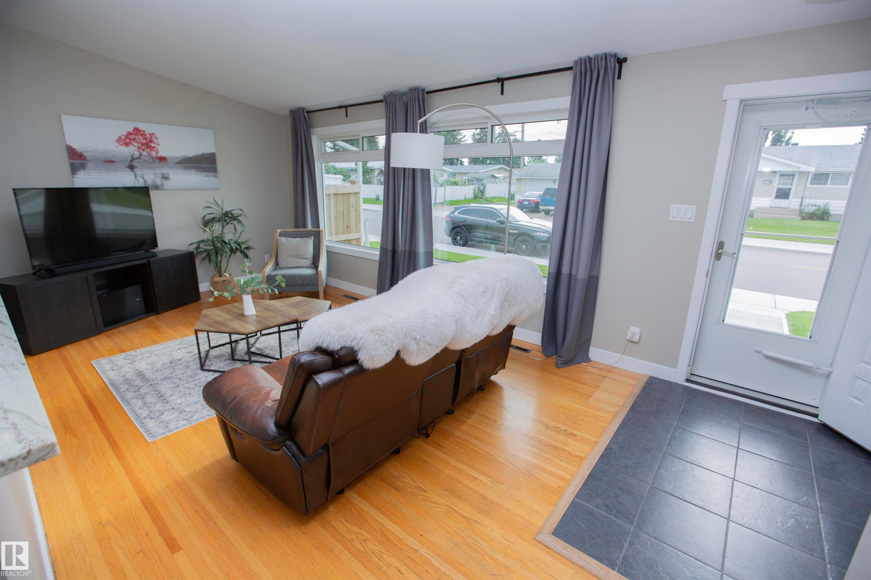 Spacious primary suite showcasing wood-finish flooring, and abundant natural light from multiple windows - 9107 58 Street Nw, Edmonton, AB - Indoor Photo Showing Living Room