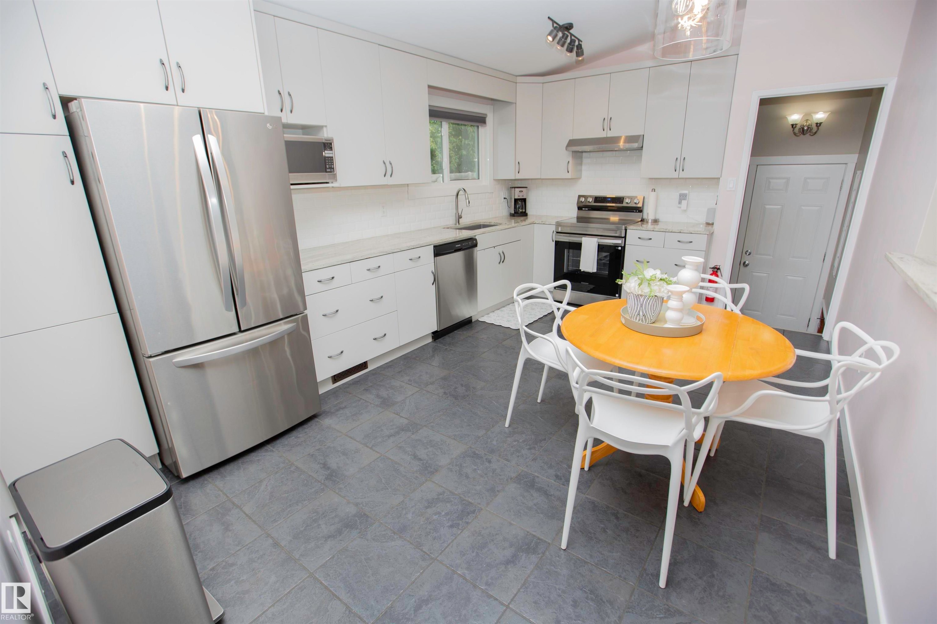 Kitchen featuring stainless steel appliances, white cabinetry, a tiled backsplash, light-toned countertops, and gray floor tiles - 9107 58 Street Nw, Edmonton, AB - Indoor