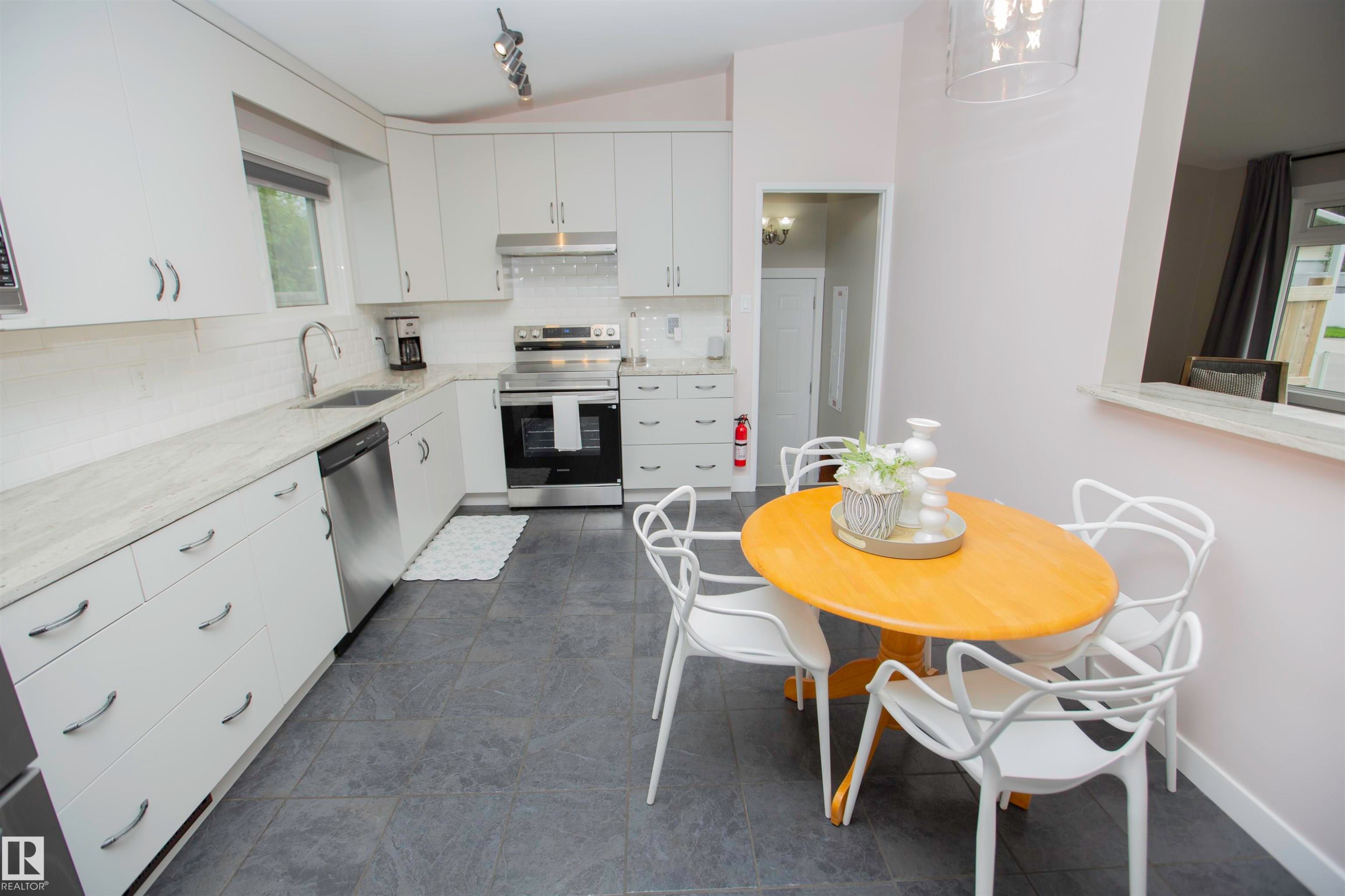 Kitchen featuring white cabinetry, light-toned countertops, stainless steel appliances, and dark tile flooring - 9107 58 Street Nw, Edmonton, AB - Indoor Photo Showing Dining Room