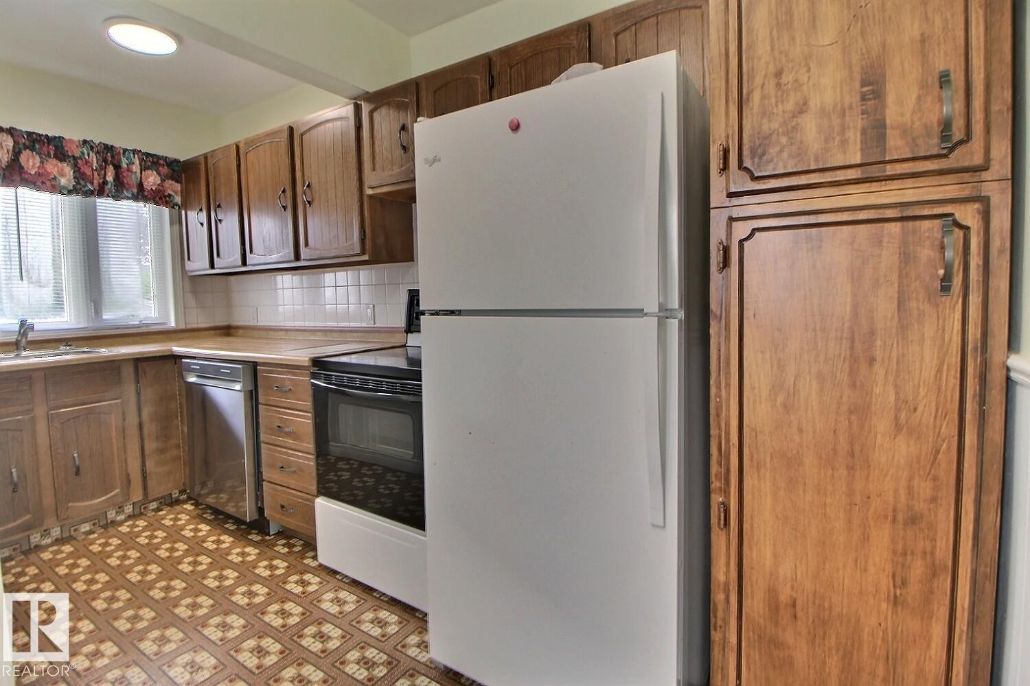 Kitchen with wood-finish cabinetry, patterned floor tiles, white tile backsplash, and a built-in dishwasher - 11336 83 Street Nw, Edmonton, AB - Indoor Photo Showing Kitchen