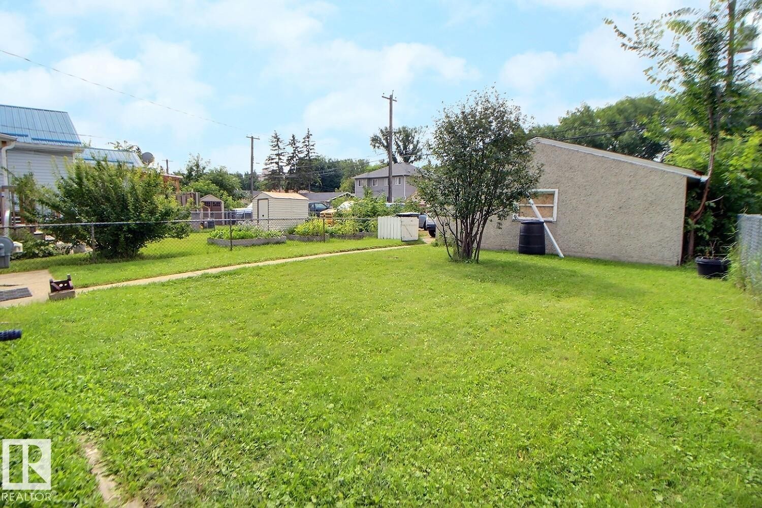 Expansive green lawn with a chain-link fence, mature shrubbery, and a visible storage shed - 11336 83 Street Nw, Edmonton, AB - Outdoor