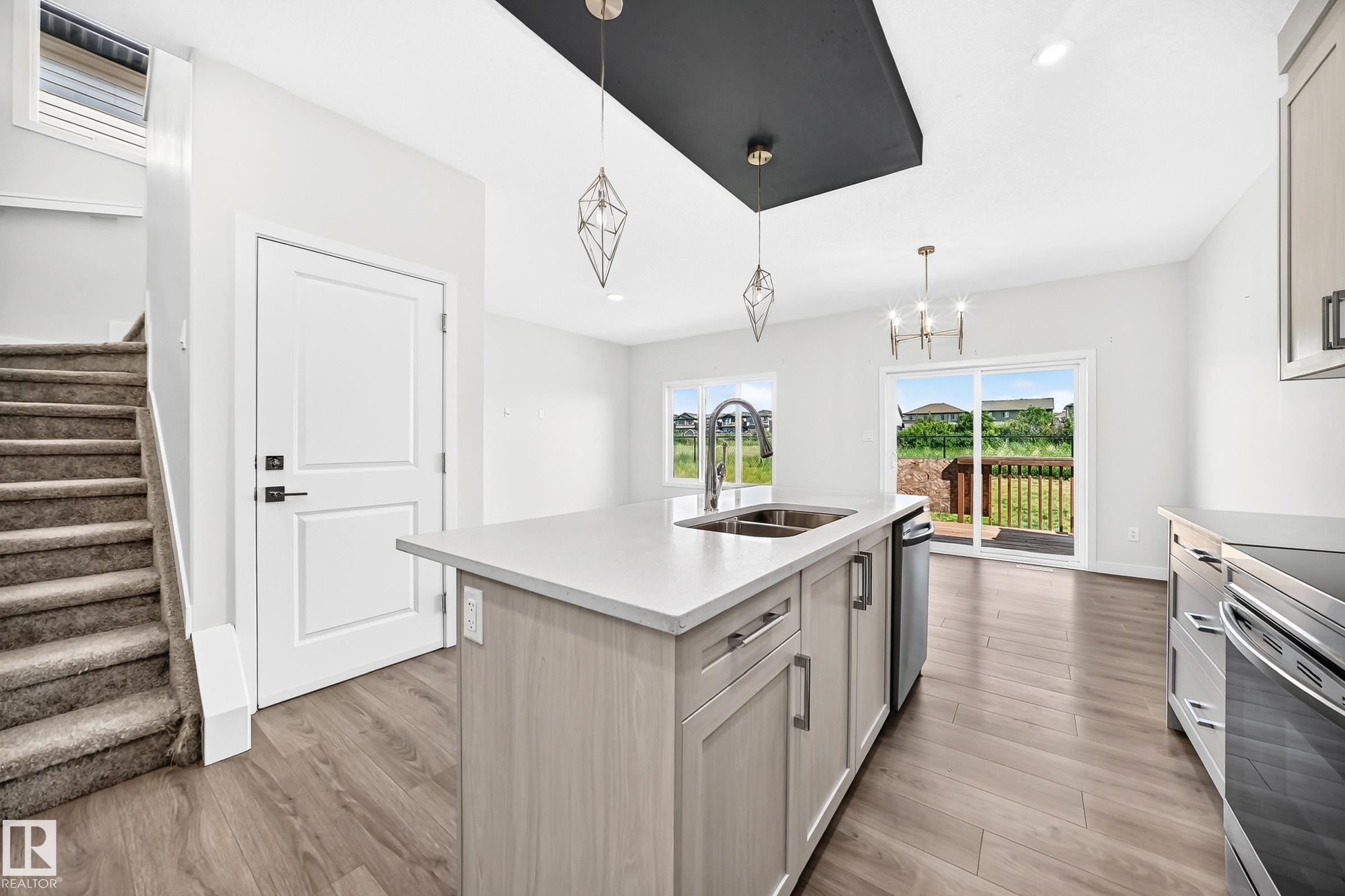 Kitchen island with integrated sink, wood-finish flooring, sliding glass door to exterior deck, and carpeted staircase - 8823 Carson Way Sw, Edmonton, AB - Indoor Photo Showing Kitchen With Double Sink With Upgraded Kitchen