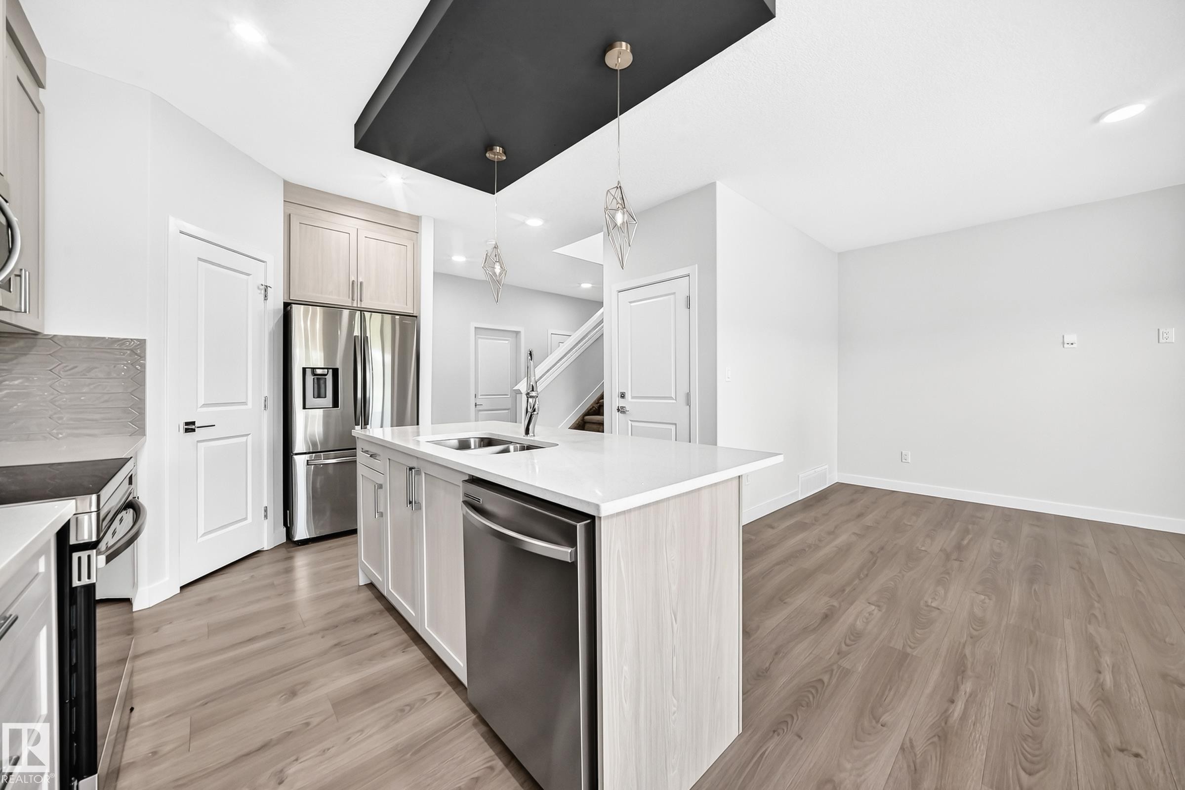 Modern kitchen featuring a central island with an undermount sink, stainless steel appliances, and light wood-finish cabinetry - 8823 Carson Way Sw, Edmonton, AB - Indoor Photo Showing Kitchen With Double Sink With Upgraded Kitchen