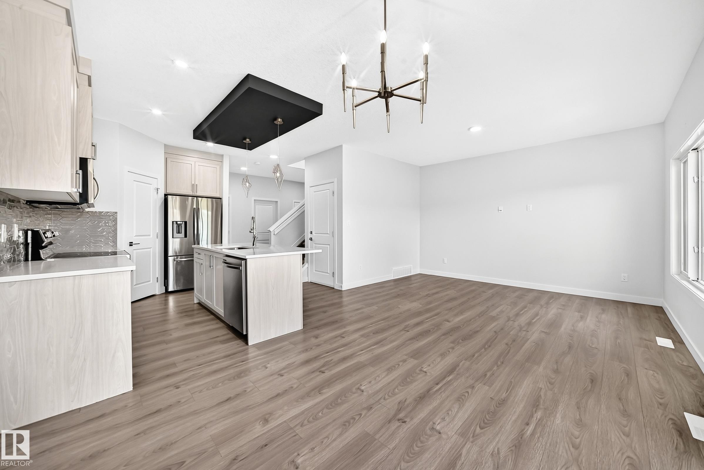 Open-concept living area featuring wood-finish flooring, a kitchen island with integrated sink, stainless steel appliances, and sleek overhead lighting - 8823 Carson Way Sw, Edmonton, AB - Indoor Photo Showing Kitchen With Upgraded Kitchen