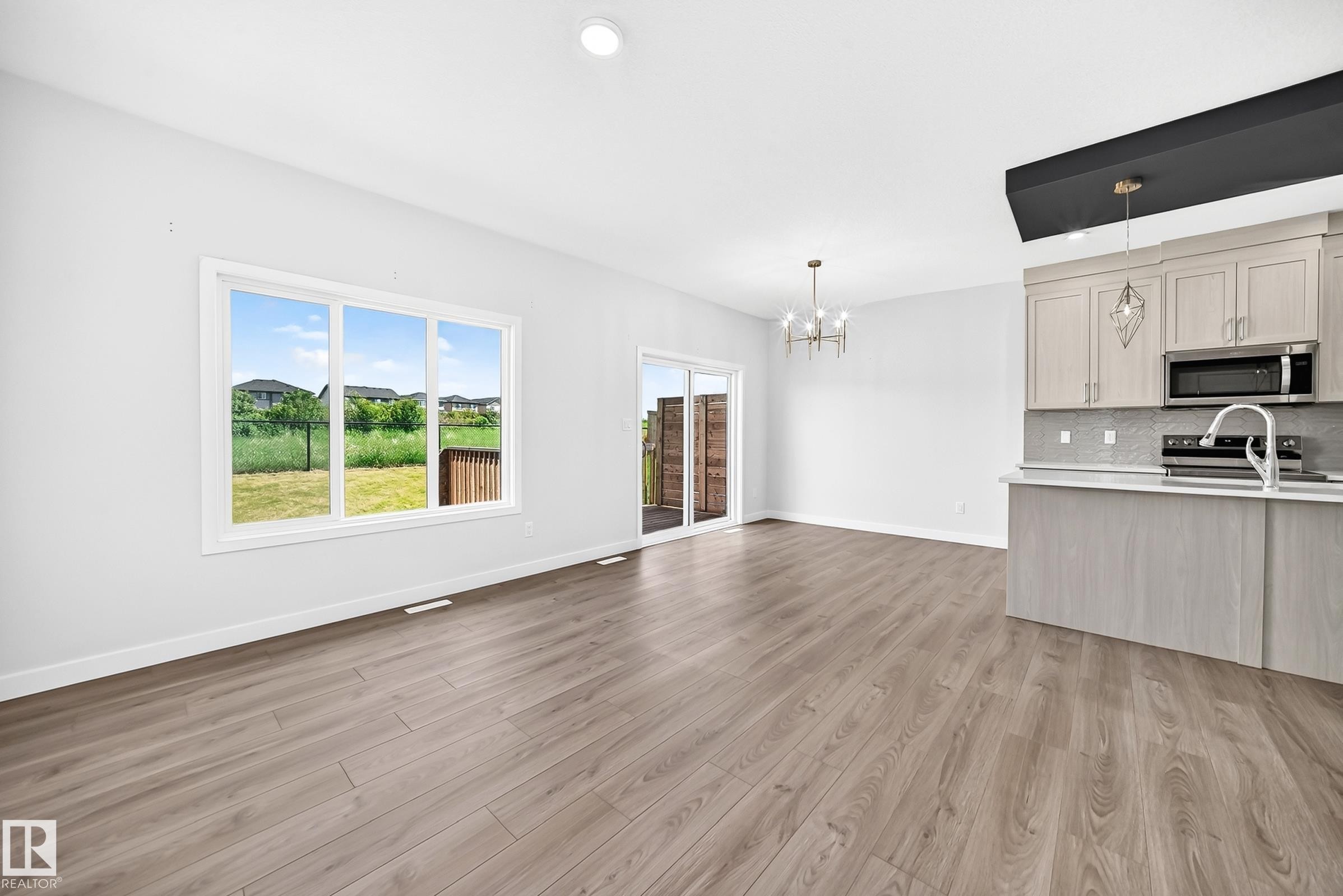 Wood-finish flooring, white walls, large window, sliding glass door, and kitchen with light-toned cabinetry - 8823 Carson Way Sw, Edmonton, AB - Indoor Photo Showing Kitchen