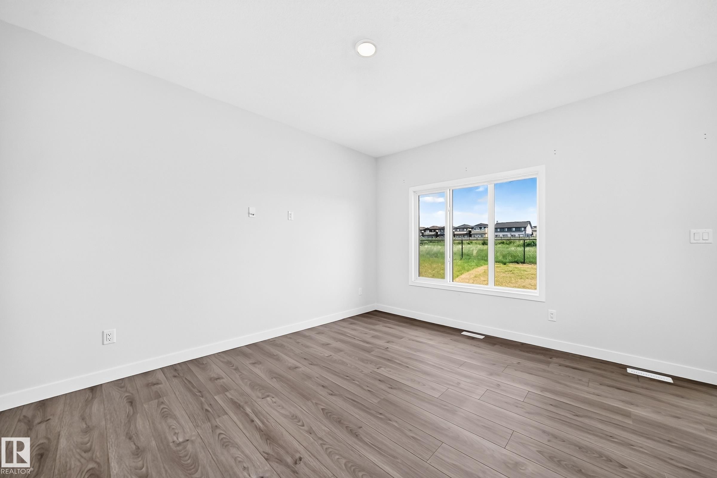 Spacious room with wood-finish flooring, white walls, and a large multi-pane window - 8823 Carson Way Sw, Edmonton, AB - Indoor Photo Showing Other Room