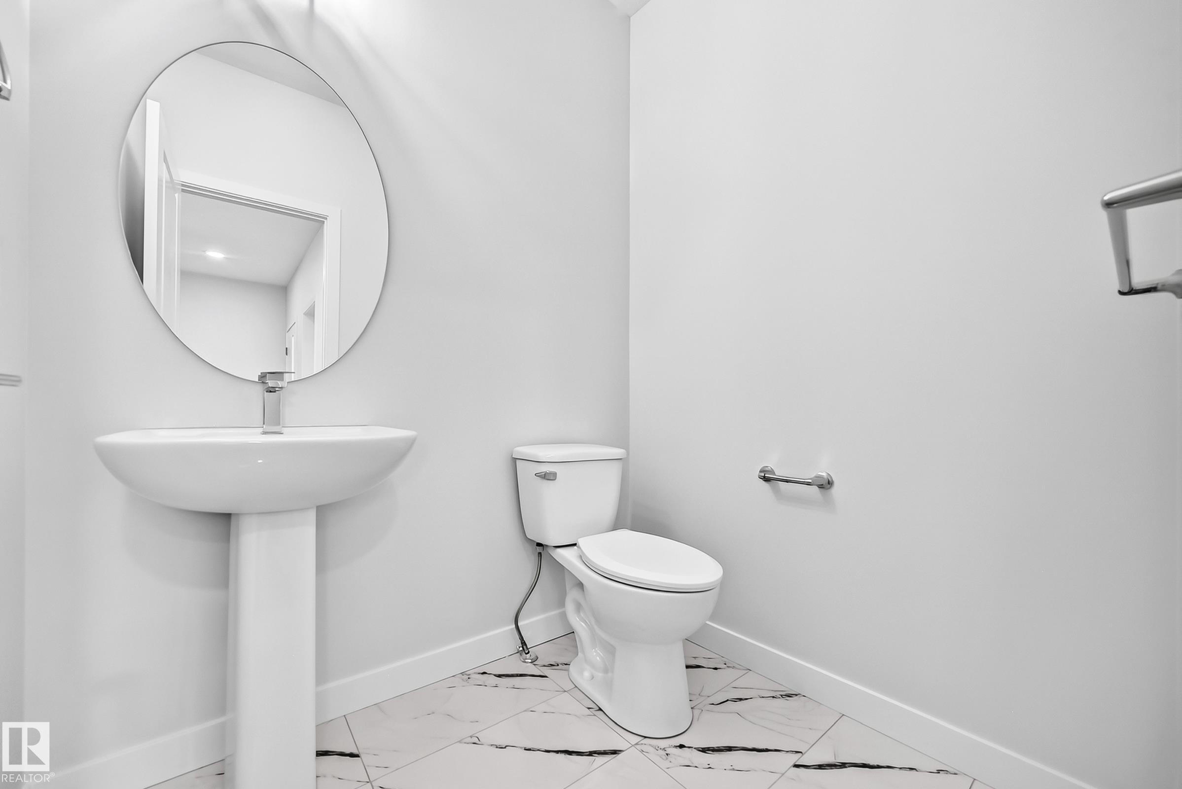 Pedestal sink with a circular mirror, modern toilet, and large format floor tiles - 8823 Carson Way Sw, Edmonton, AB - Indoor Photo Showing Bathroom