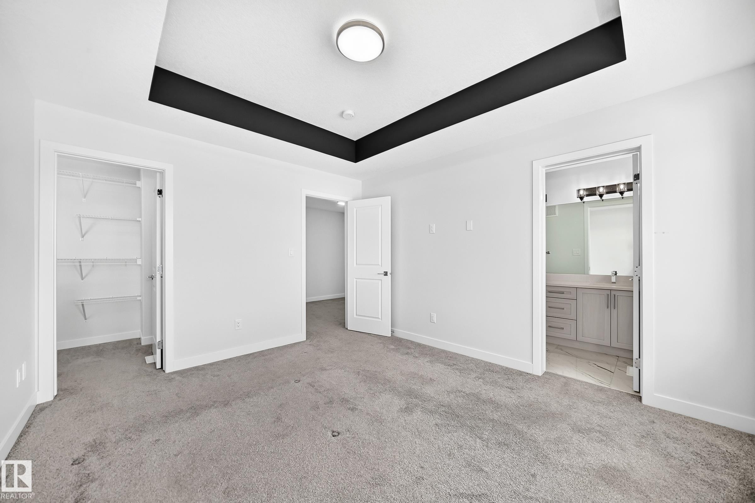 Tray ceiling with accent trim, carpeted flooring, built-in closet shelving, and an en-suite bathroom with a vanity and mirror - 8823 Carson Way Sw, Edmonton, AB - Indoor Photo Showing Other Room