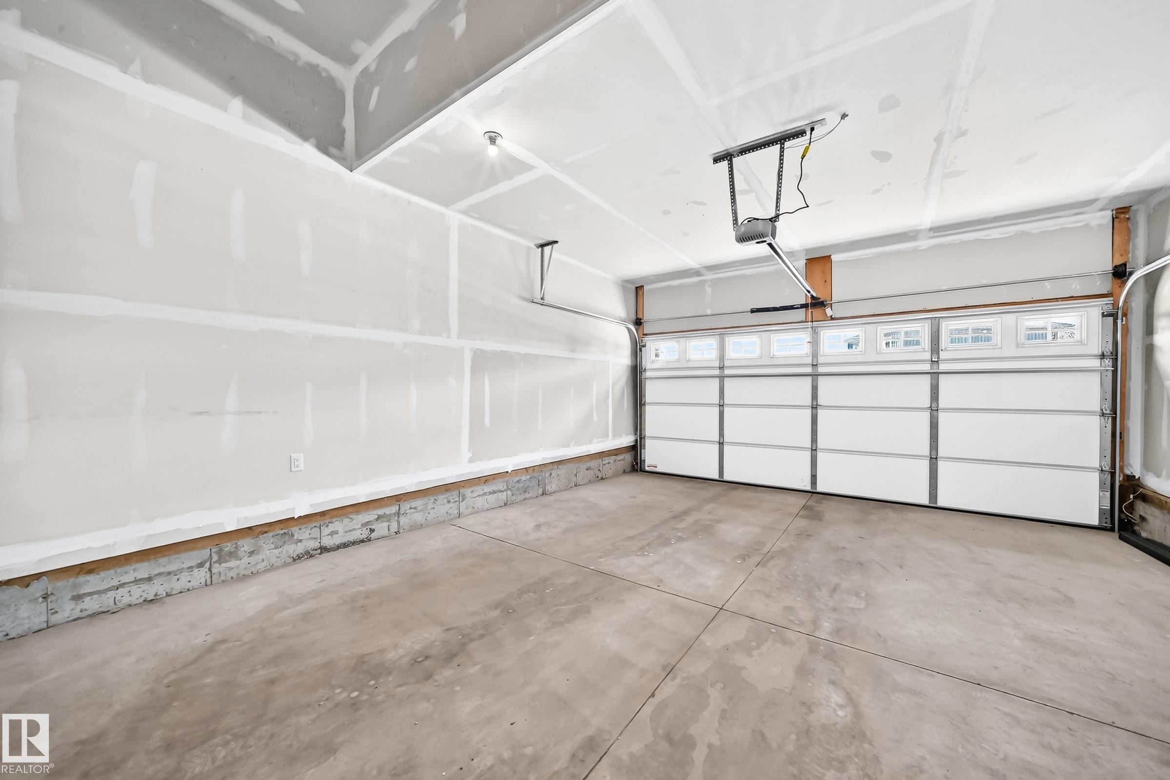 Spacious garage featuring a concrete floor, overhead lighting, and an automated garage door with upper-level windows - 8823 Carson Way Sw, Edmonton, AB - Indoor Photo Showing Garage