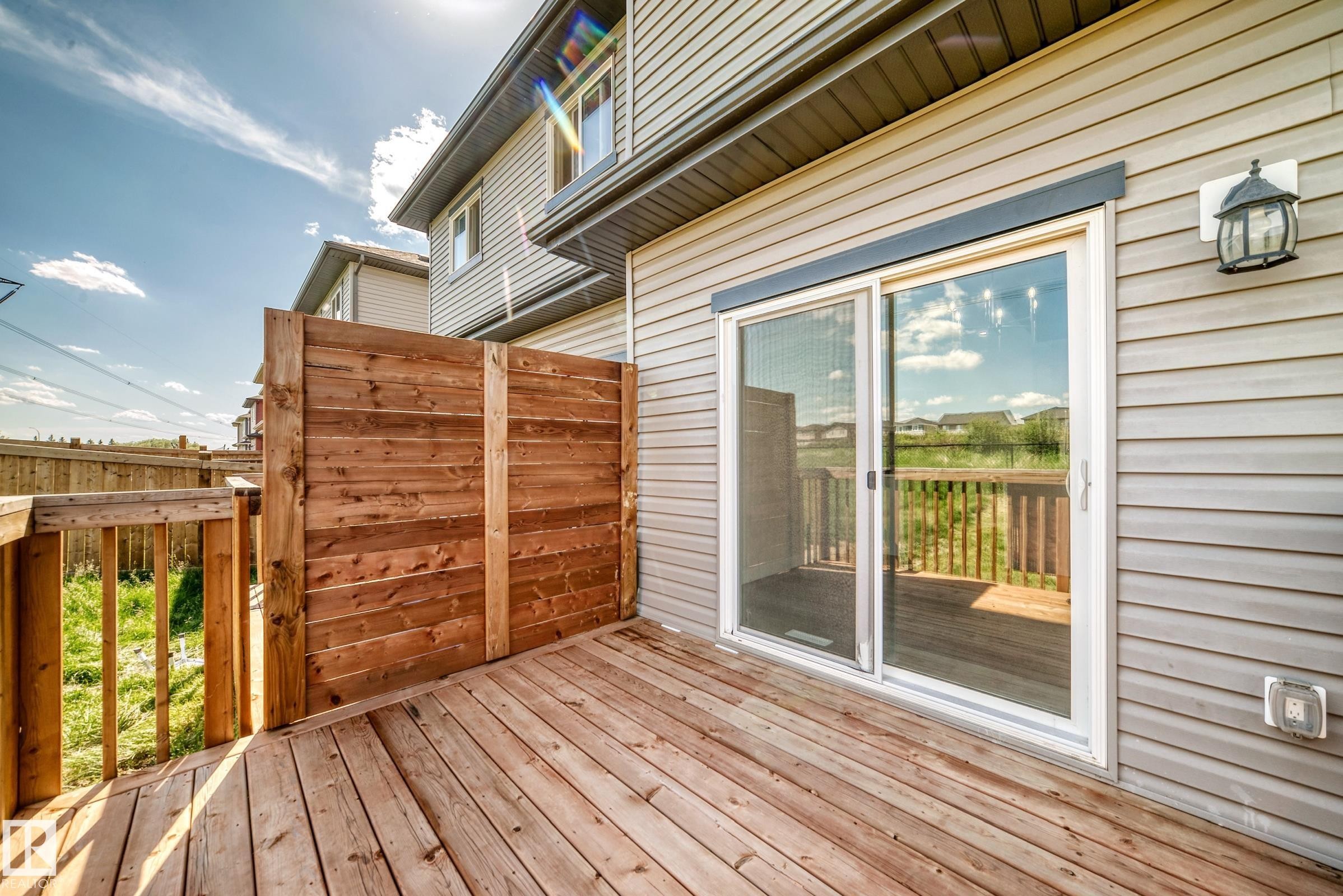 Wood-finish deck with privacy wall, sliding glass door, and exterior lighting fixture - 8823 Carson Way Sw, Edmonton, AB - Outdoor With Deck Patio Veranda With Exterior