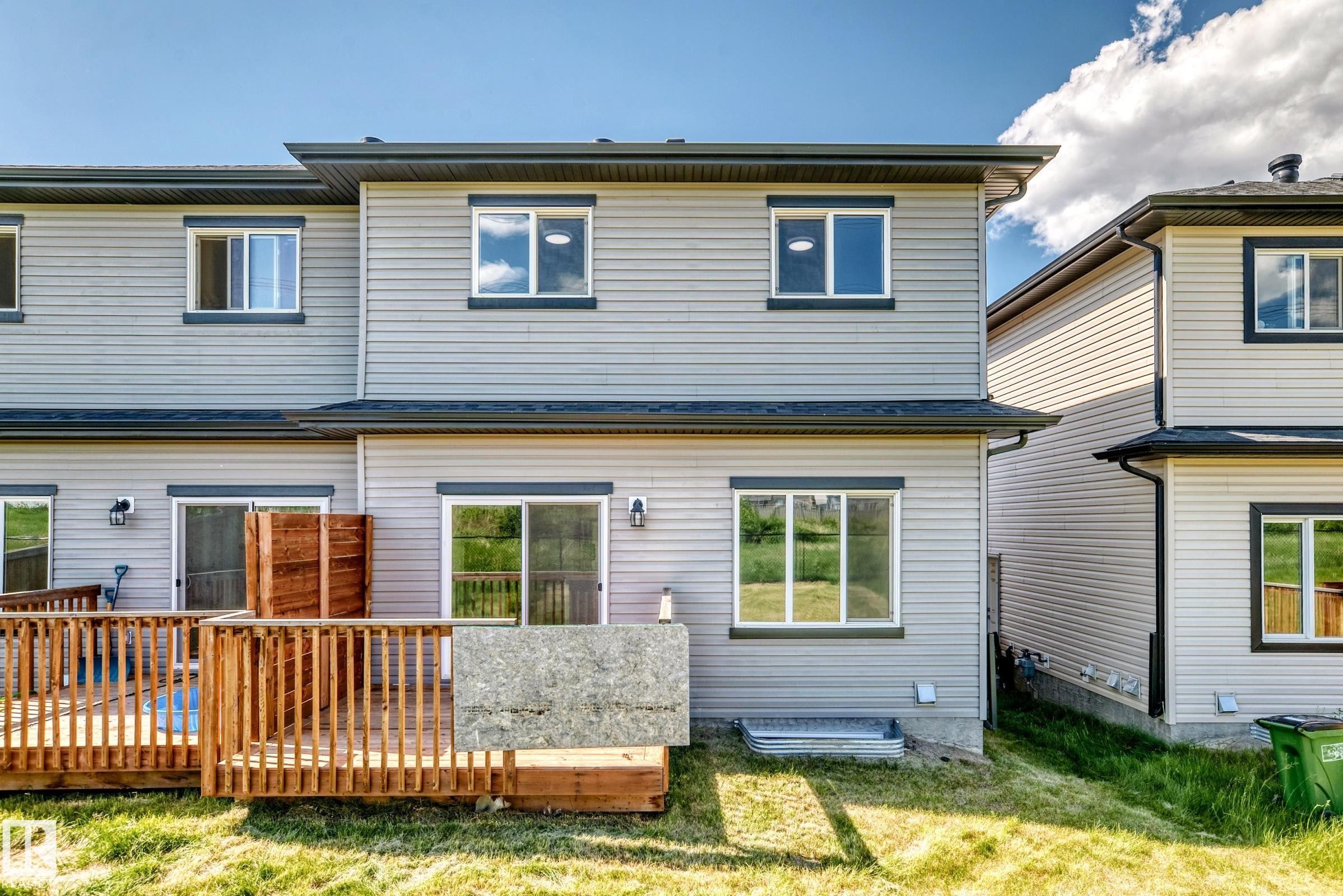 Rear exterior featuring light grey siding, multiple windows with dark trim, a wooden deck with railings, and two sliding glass doors - 8823 Carson Way Sw, Edmonton, AB - Outdoor With Exterior
