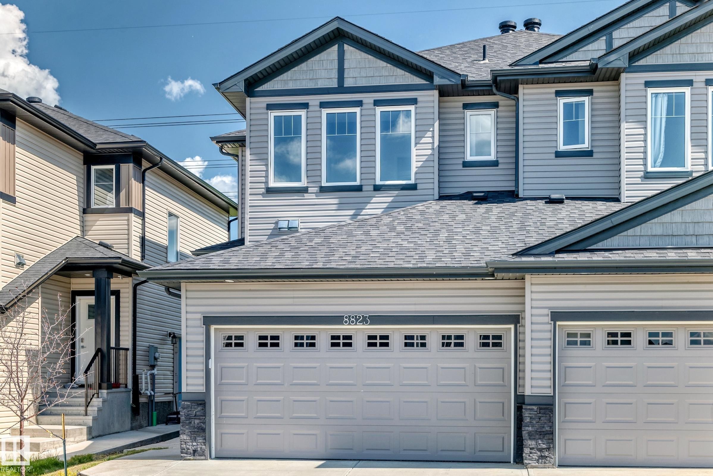 Gray siding exterior with dark trim accents, multiple gables, a two-car garage with transom windows, and an asphalt shingle roof - 8823 Carson Way Sw, Edmonton, AB - Outdoor