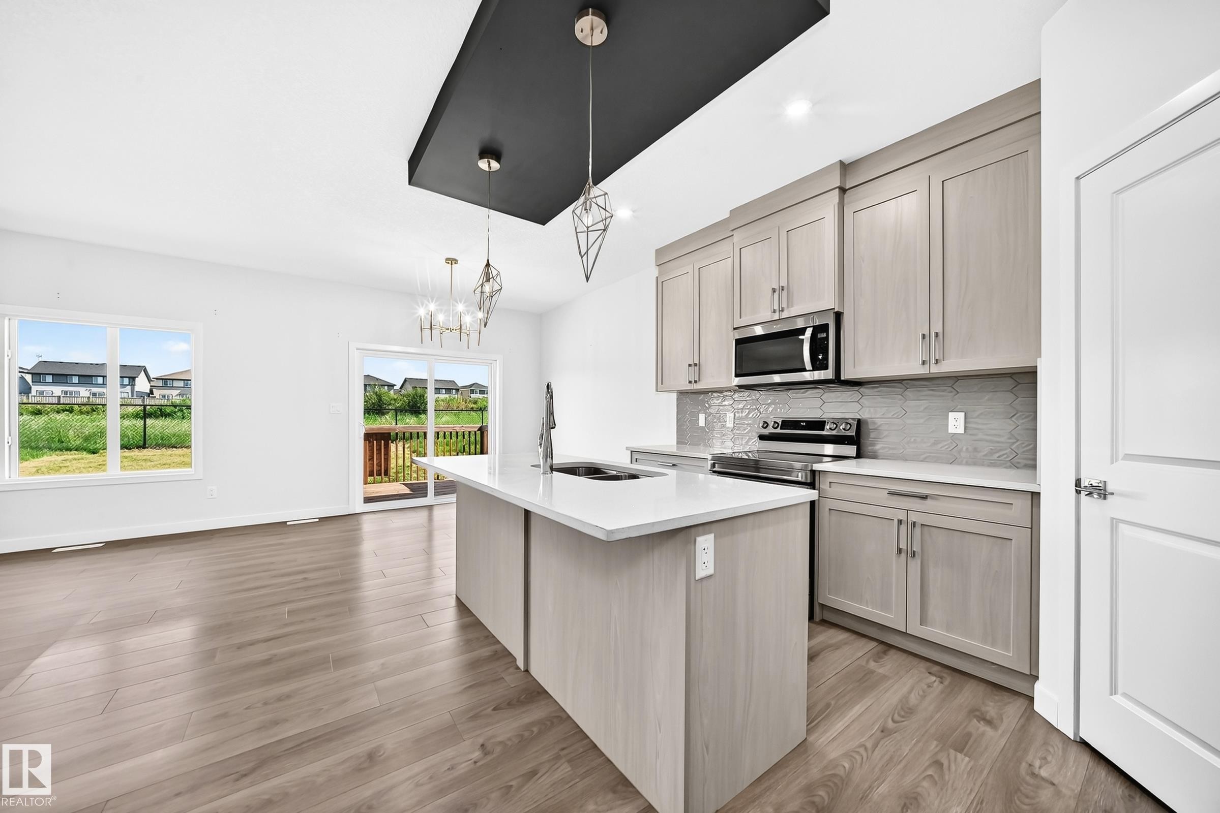 Modern kitchen featuring light wood-finish cabinetry, stainless steel appliances, a center island with a white countertop, and a geometric tile backsplash - 8823 Carson Way Sw, Edmonton, AB - Indoor Photo Showing Kitchen With Upgraded Kitchen