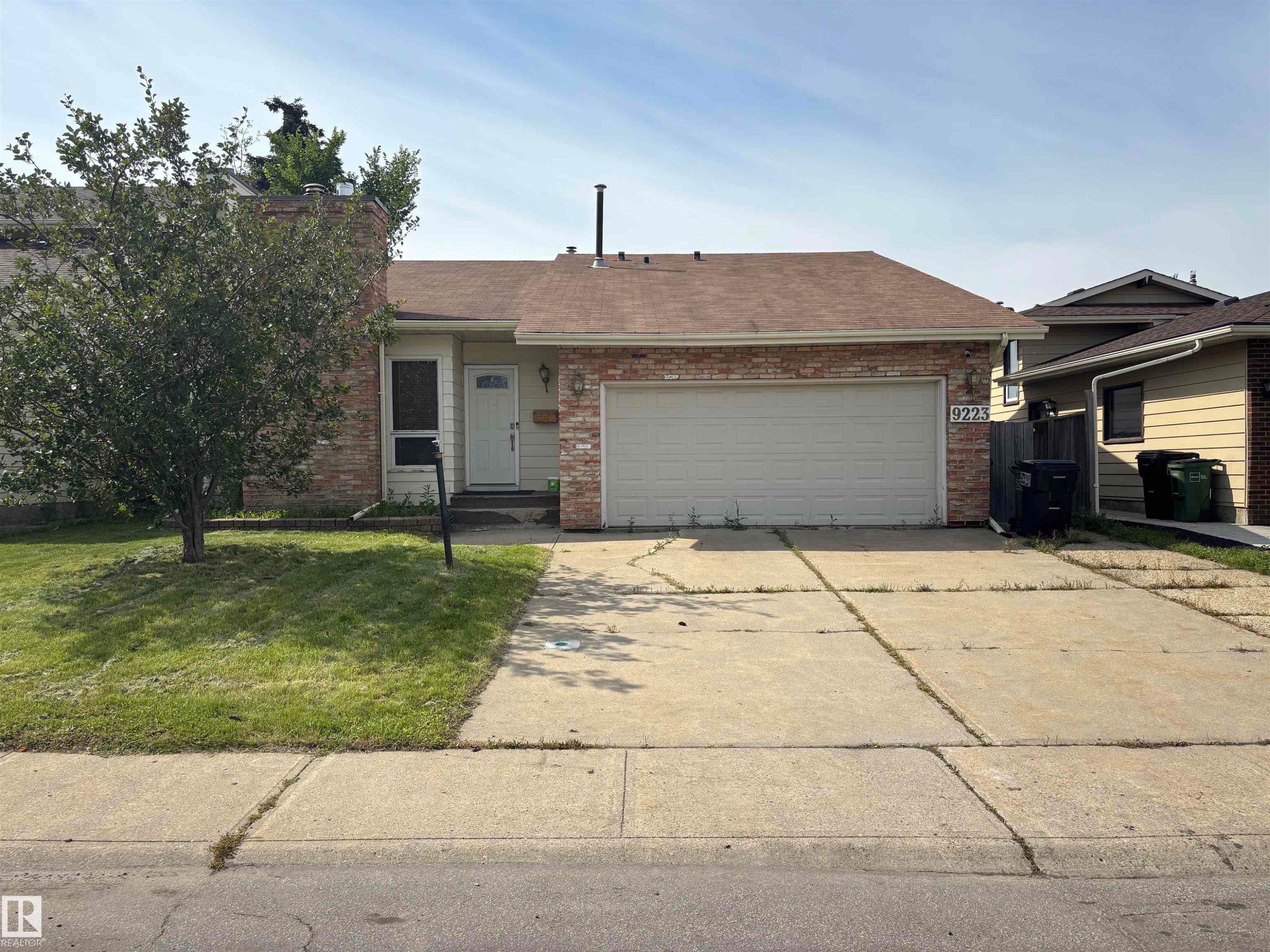 Brick facade, attached garage, concrete driveway, front entry with storm door, and a manicured lawn - 9223 172 Avenue Nw, Edmonton, AB