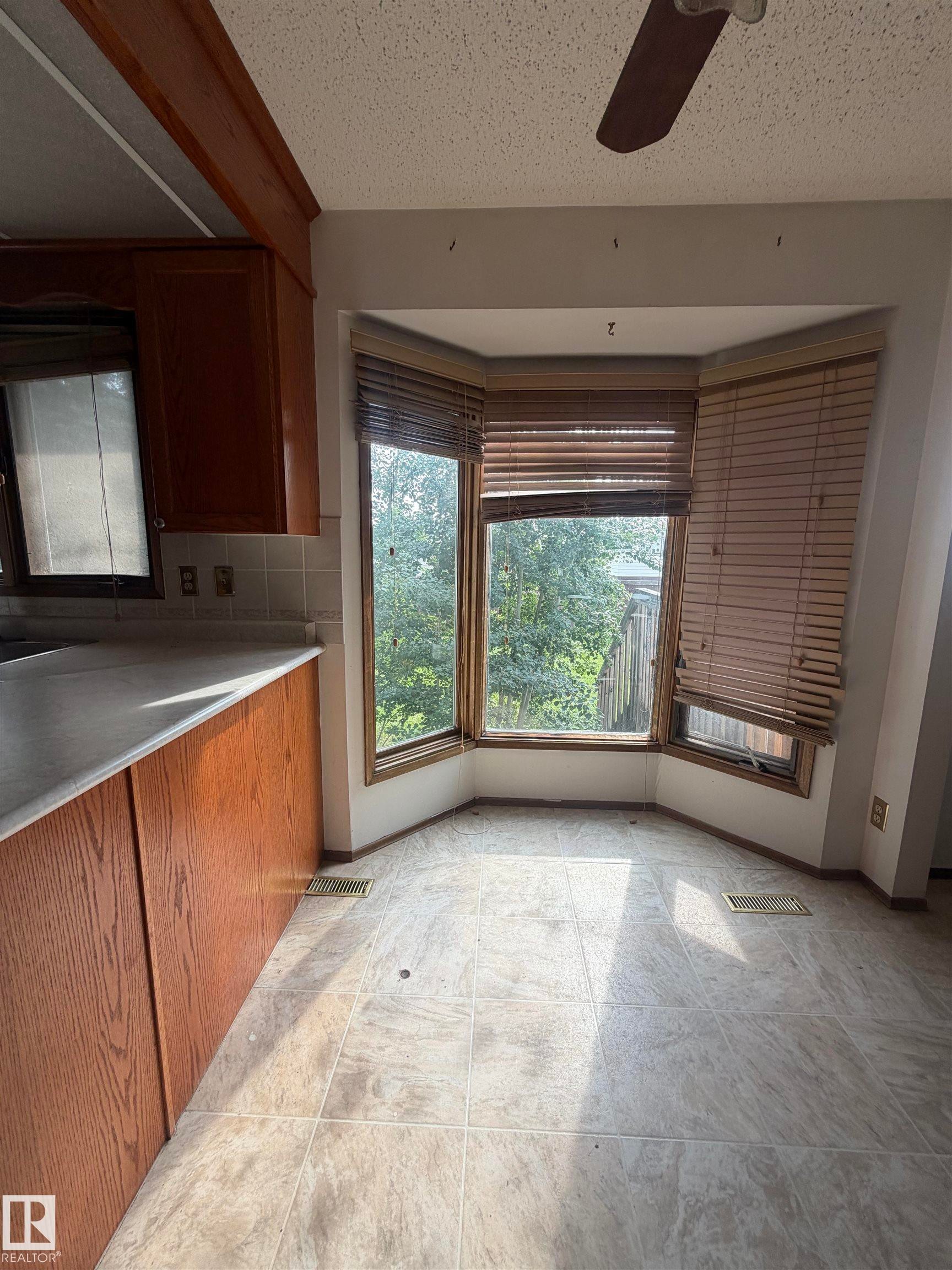 Bay window with wood-finish blinds, wood-finish cabinetry, and a light-toned countertop - 9223 172 Avenue Nw, Edmonton, AB