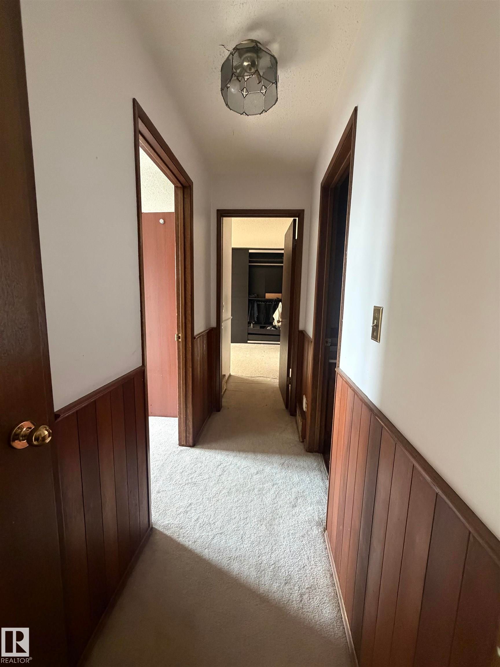 Hallway featuring dark wood-finish doors with brass hardware, neutral wall-to-wall carpeting, and wainscoting detail along lower walls - 9223 172 Avenue Nw, Edmonton, AB