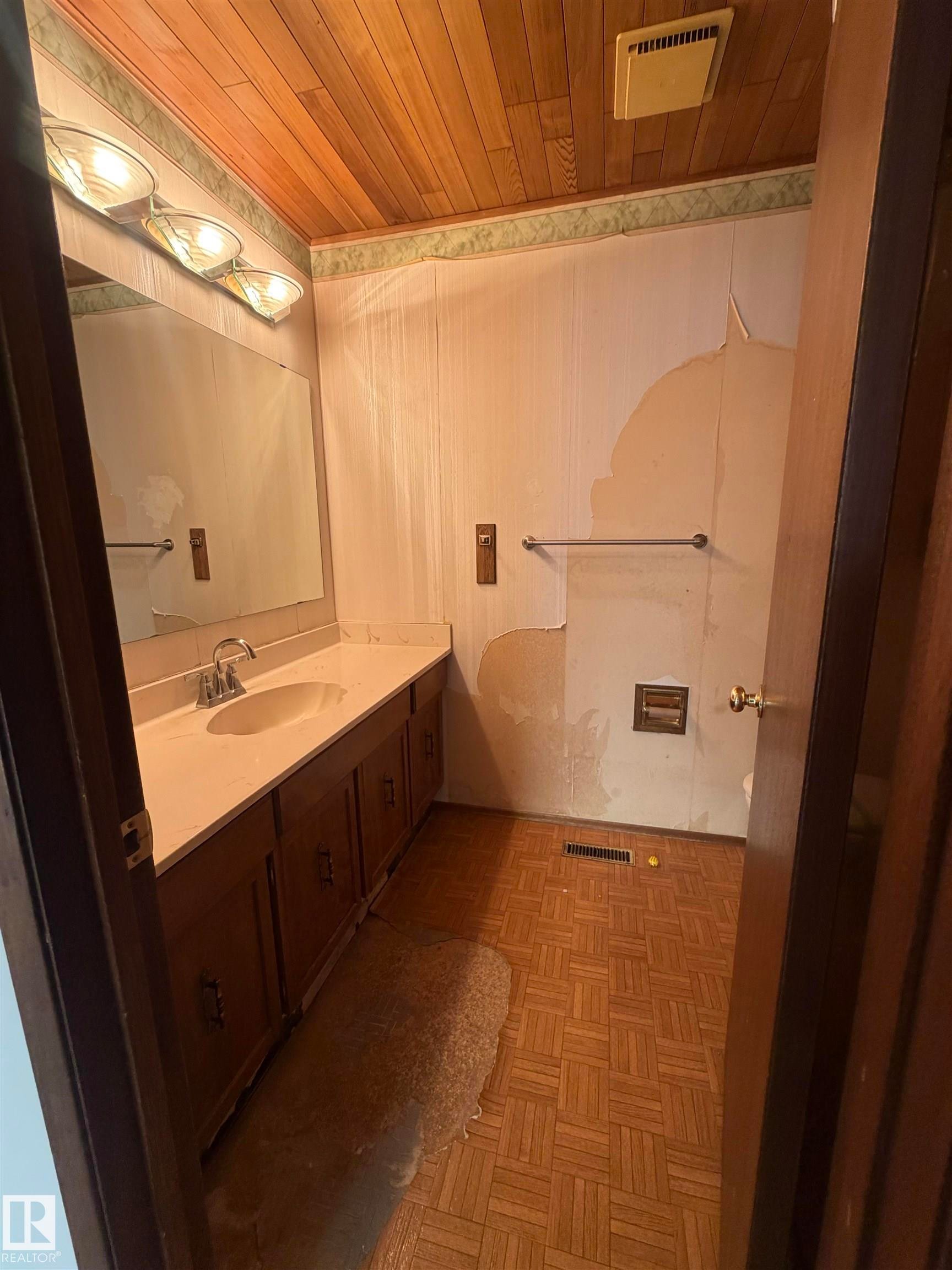 Master bathroom featuring dual vanity with dark cabinetry and countertop, framed mirror with integrated lighting, ceramic tile shower enclosure with glass partition and chrome fixtures, and herringbone wood-finish flooring throughout - 9223 172 Avenue Nw, Edmonton, AB