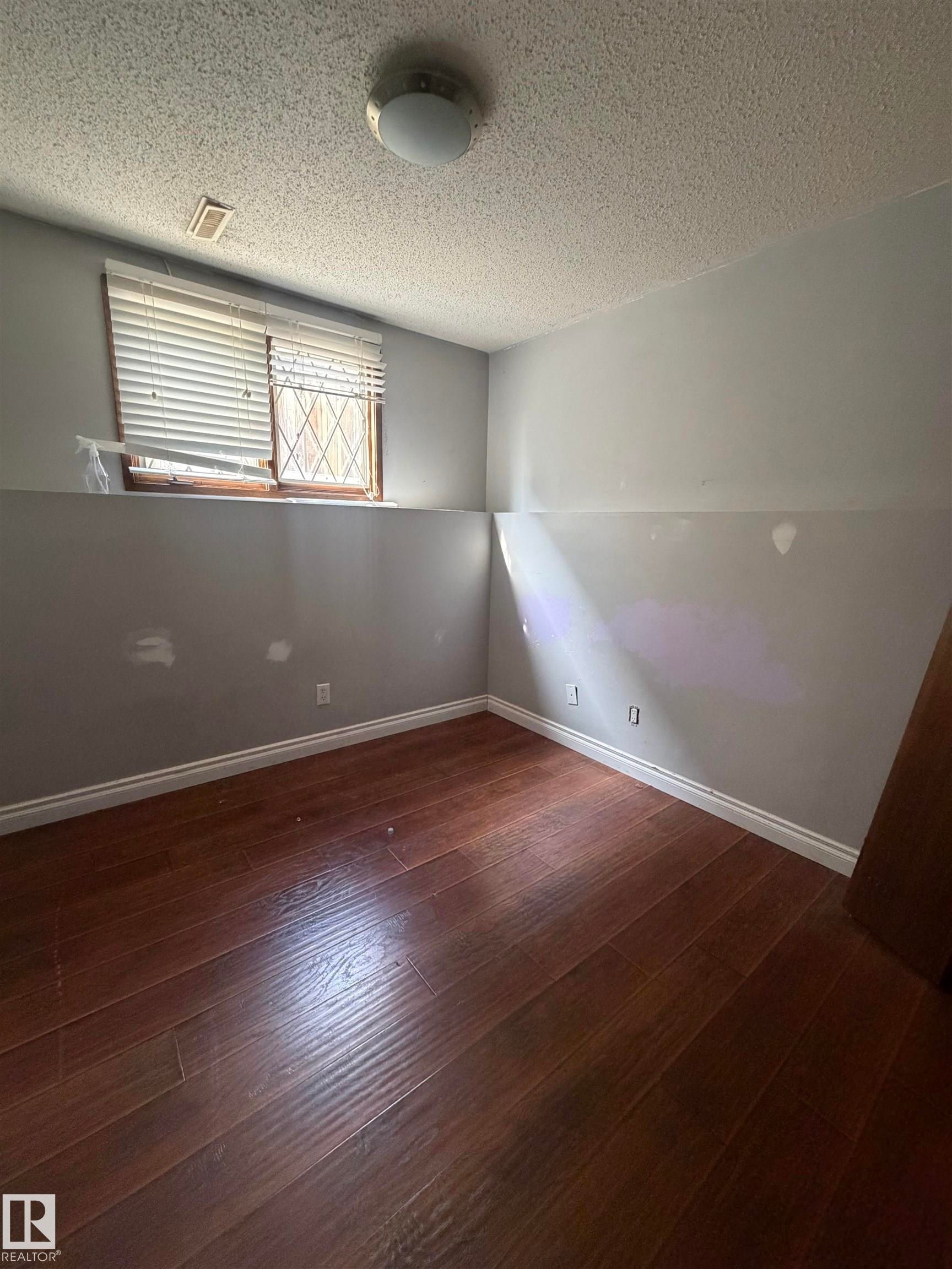 Wood-finish flooring with white baseboards, a flush-mount ceiling light fixture, and a window with blinds - 9223 172 Avenue Nw, Edmonton, AB