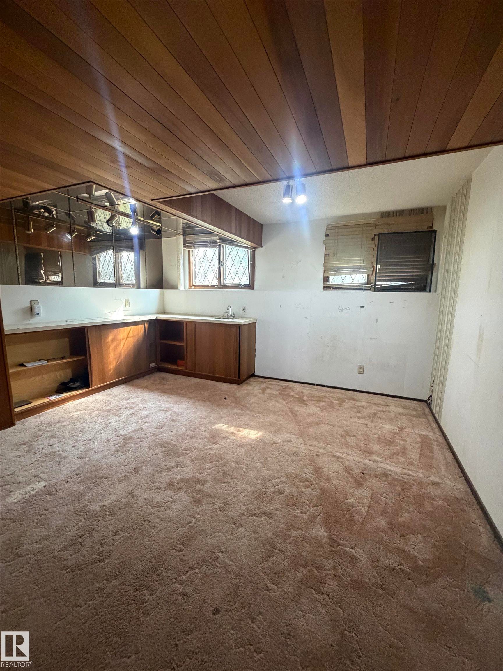 Open living area featuring wood-finish vaulted ceiling, built-in cabinetry with glass-front upper storage, wood-tone base cabinets, and carpeted flooring throughout - 9223 172 Avenue Nw, Edmonton, AB