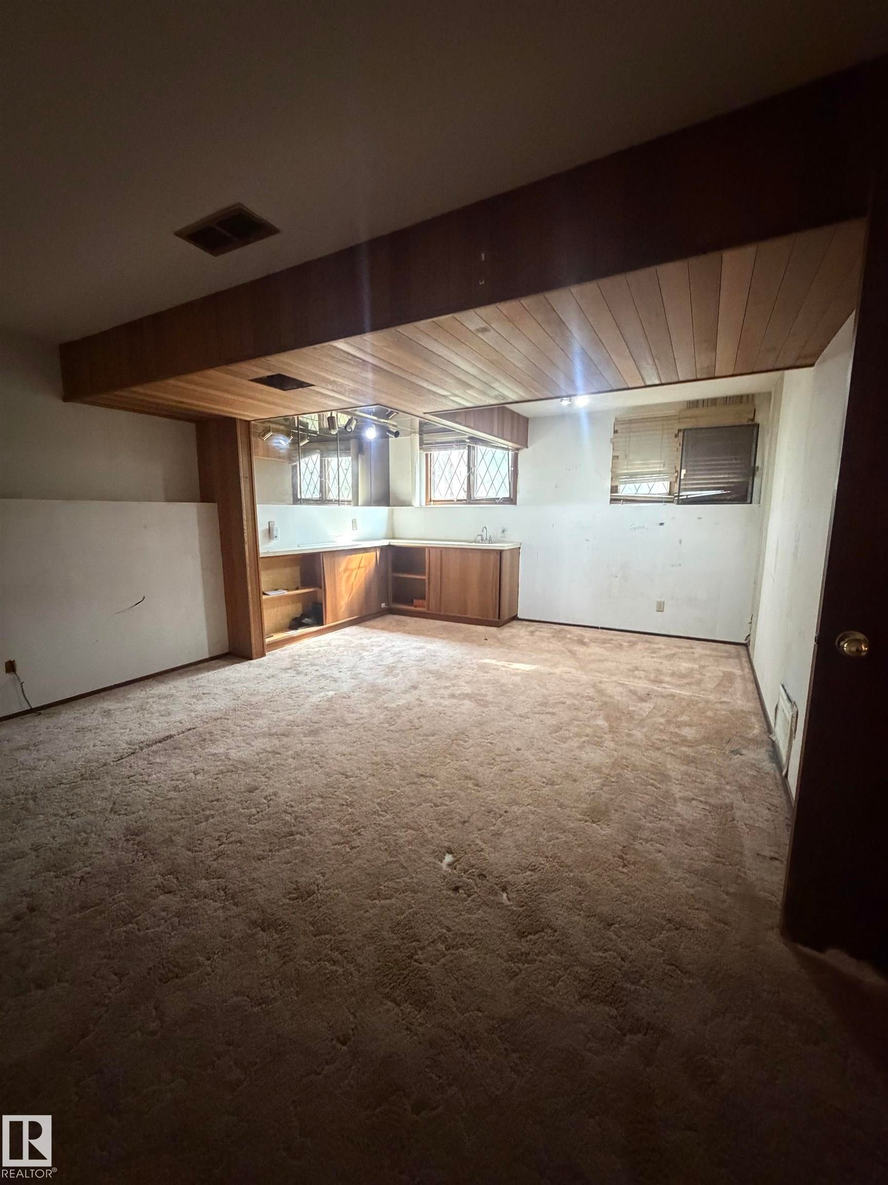 Spacious open-concept room featuring exposed wood-beam ceiling, recessed lighting, carpet flooring, and built-in cabinetry with wood finishes - 9223 172 Avenue Nw, Edmonton, AB