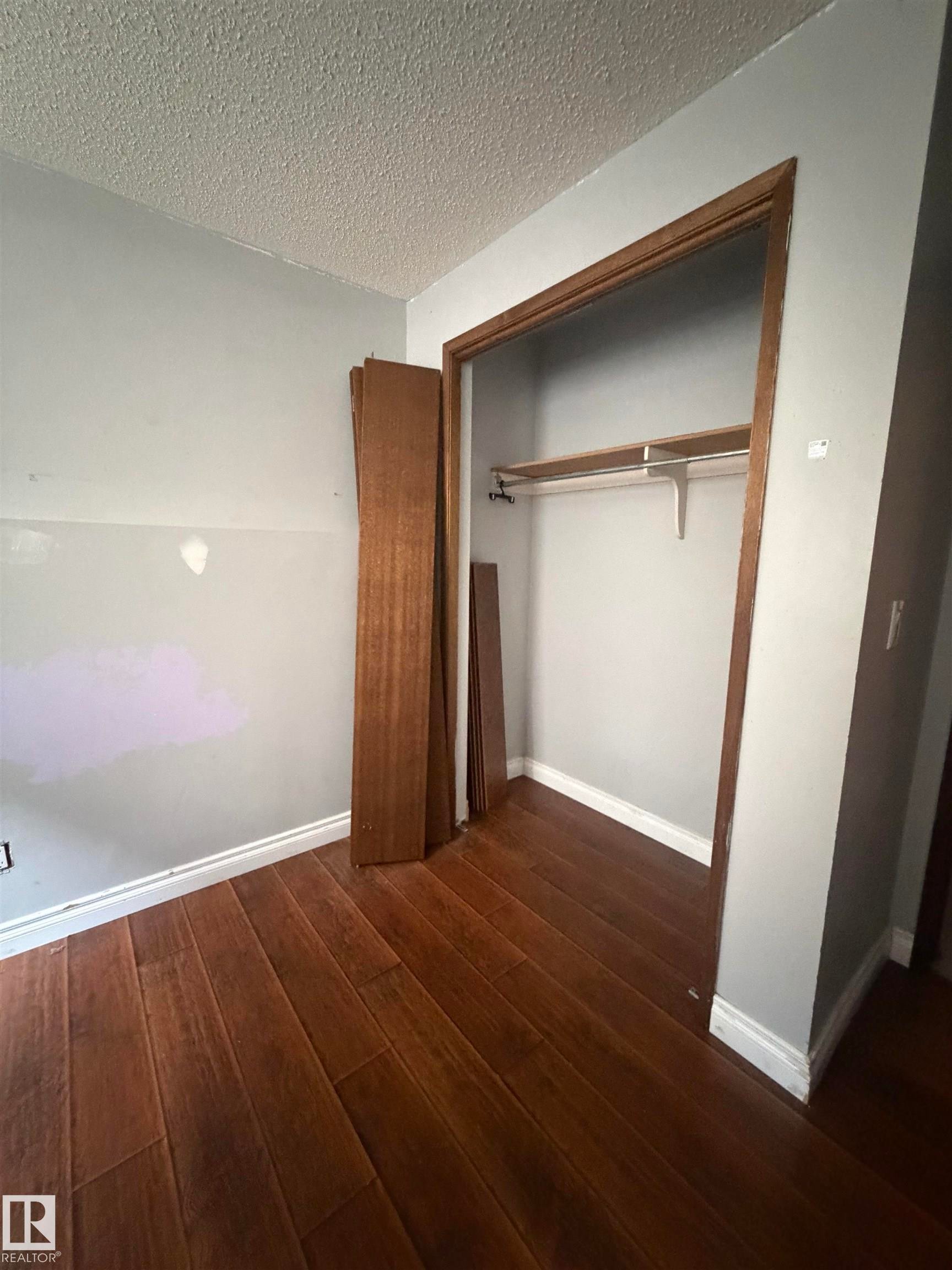 Spacious bedroom featuring rich wood-finish flooring, white painted walls, and a generous walk-in closet with wooden framing and built-in hanging rod - 9223 172 Avenue Nw, Edmonton, AB
