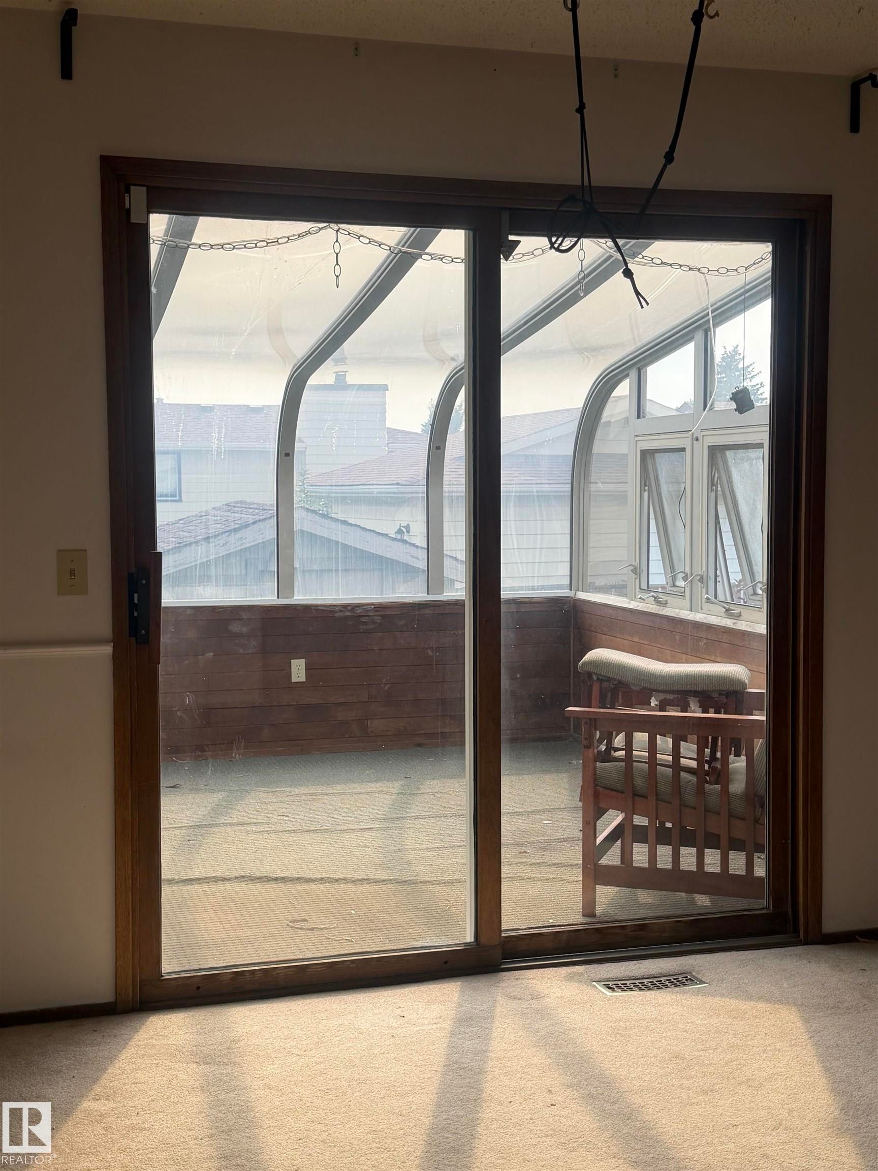 Sliding glass doors with dark wood frames opening to a covered outdoor space featuring exposed beam ceiling, metal railings, and wood-finish decking - 9223 172 Avenue Nw, Edmonton, AB