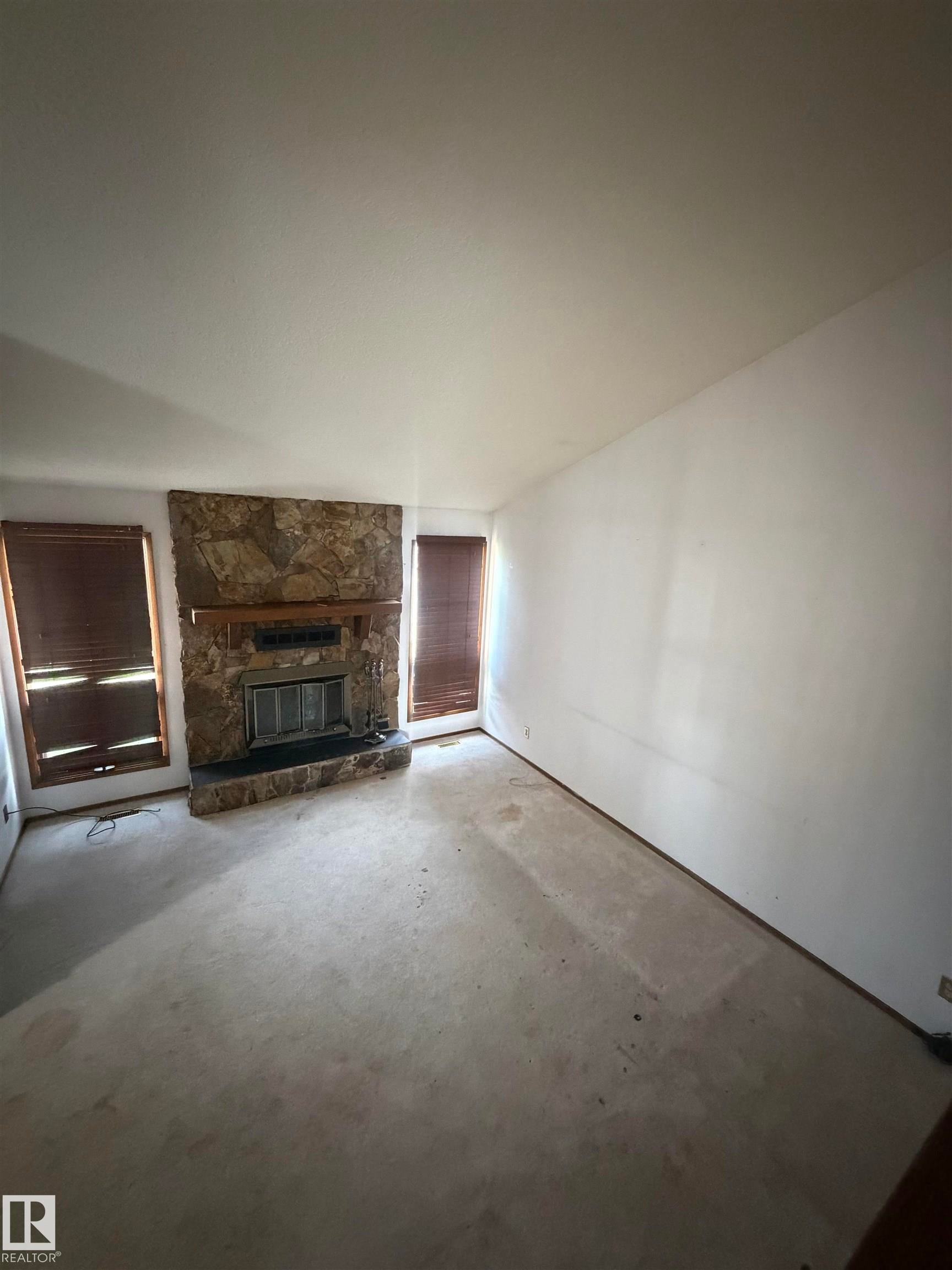 Spacious living area featuring a stone fireplace with integrated hearth, vaulted ceiling, and abundant natural light from multiple windows - 9223 172 Avenue Nw, Edmonton, AB