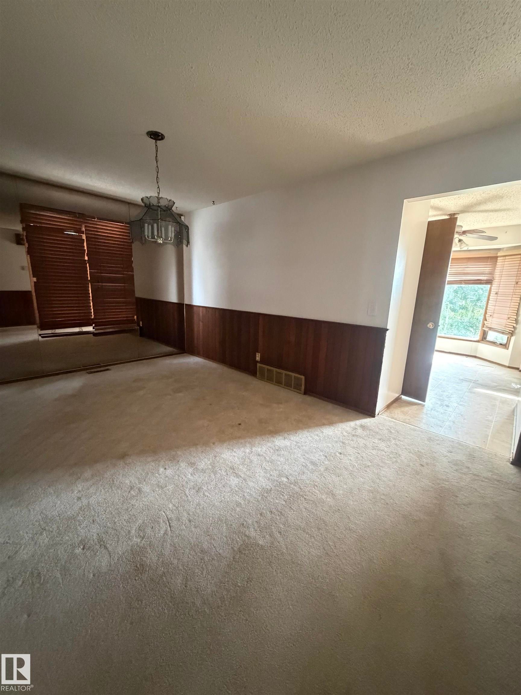 Spacious living area featuring two-tone wainscoting with wood-finish lower walls and neutral upper walls, pendant lighting, and direct access to adjoining rooms through multiple doorways - 9223 172 Avenue Nw, Edmonton, AB