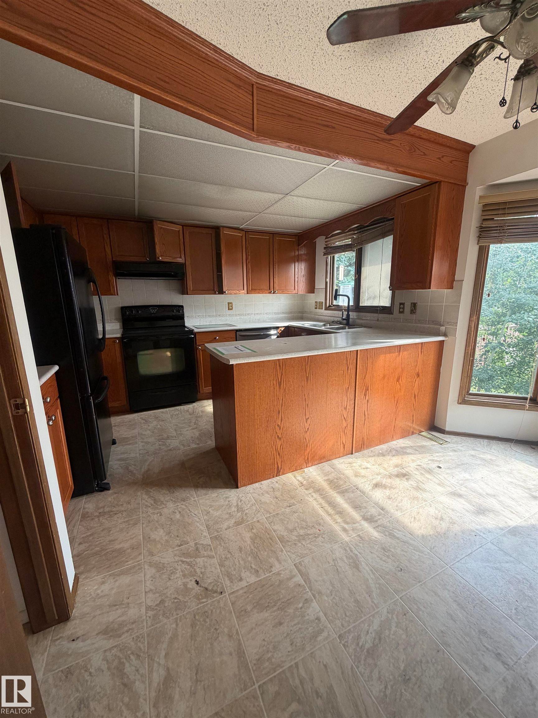 Spacious kitchen featuring wood-finish cabinetry, a center island with countertop seating, stainless steel appliances, and tile flooring throughout - 9223 172 Avenue Nw, Edmonton, AB