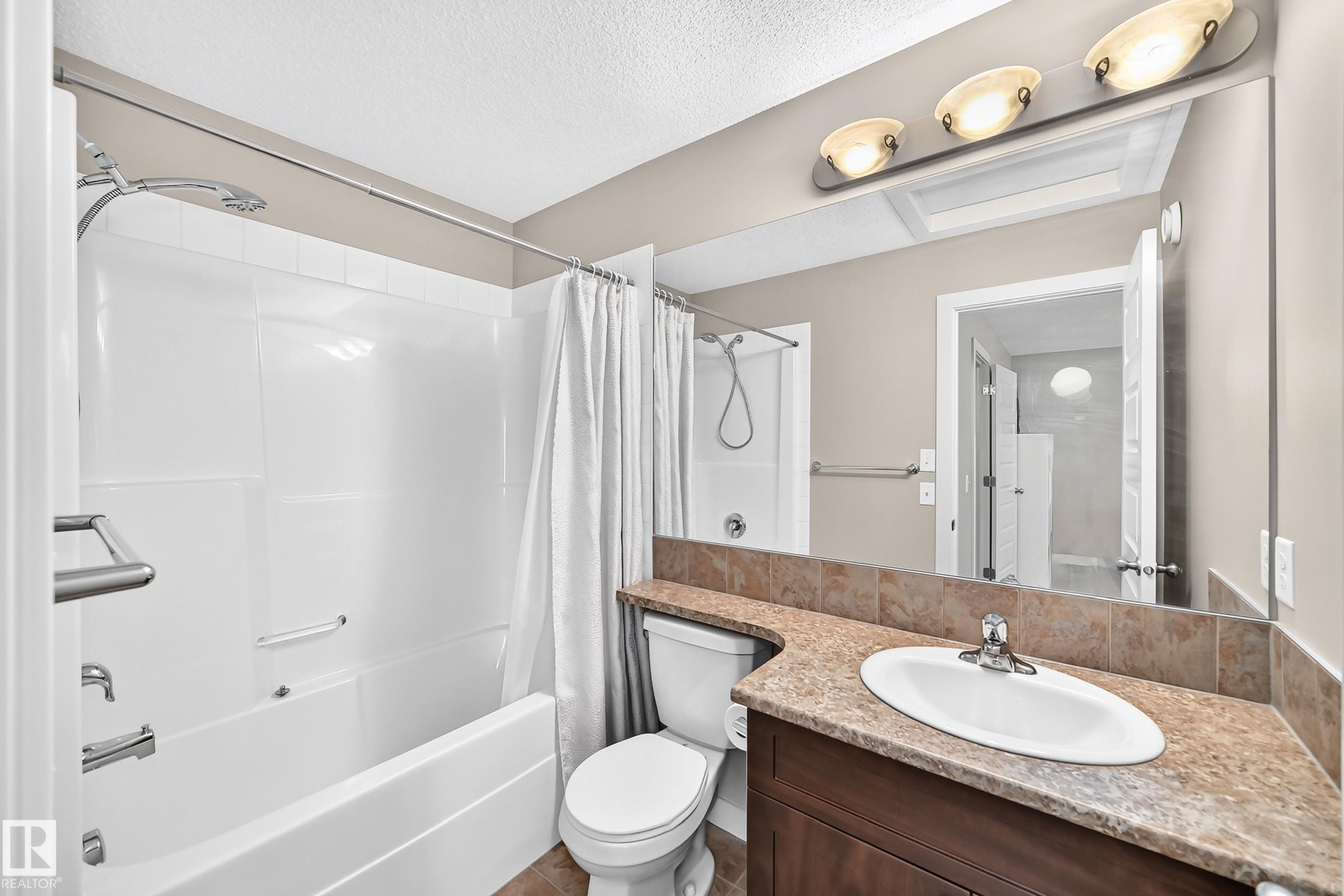 Bathroom featuring a full tub/shower combination with a white surround, a vanity with a brown countertop, an undermount sink, a large mirror, and recessed lighting - 466 Chappelle Drive Sw, Edmonton, AB - Indoor Photo Showing Bathroom