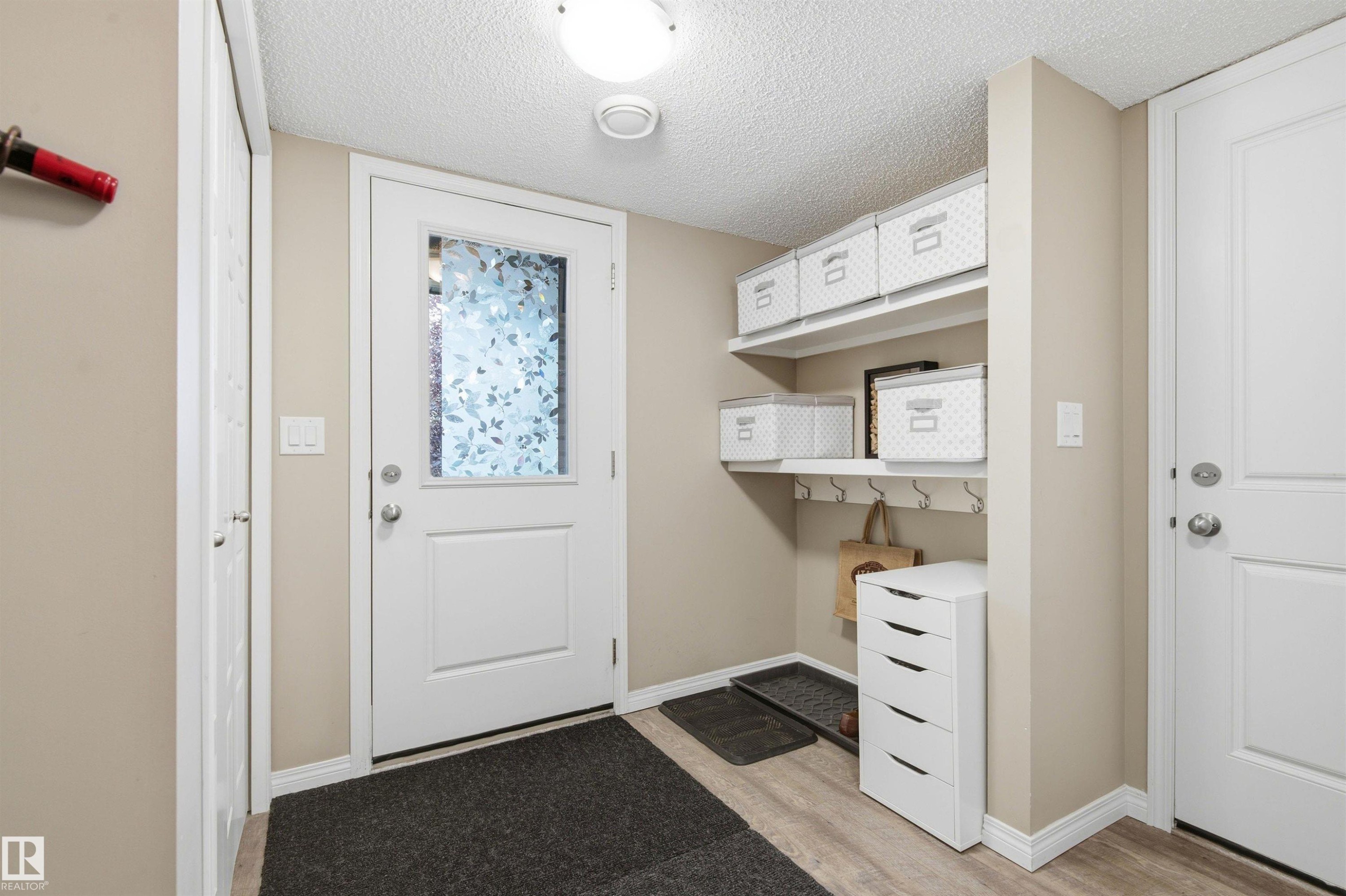 Entryway featuring a white door with a privacy glass insert, wood-finish flooring, and a built-in shelving unit with hooks - 20127 19 Avenue Nw, Edmonton, AB - Indoor Photo Showing Other Room