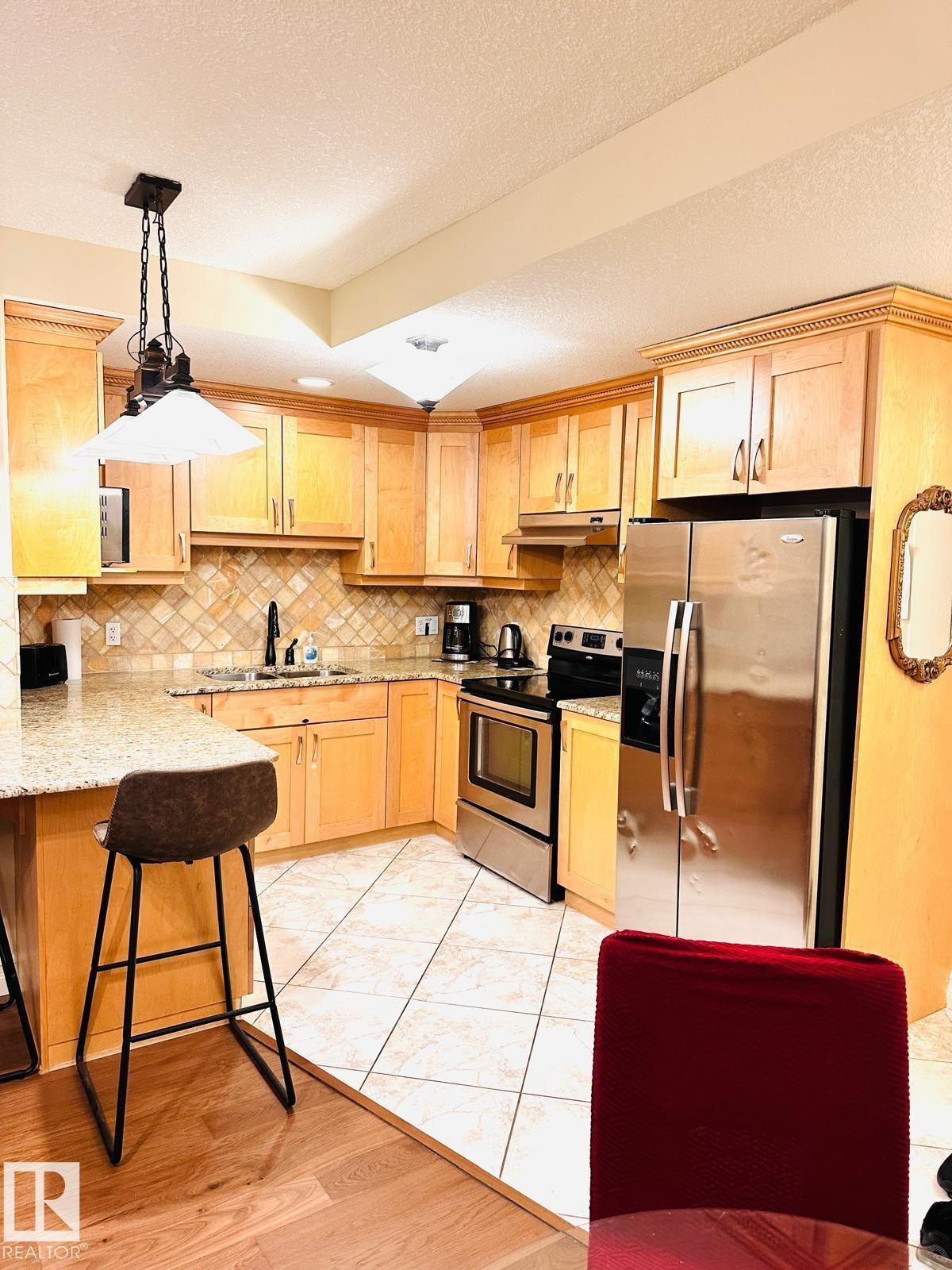 Kitchen featuring wood-finish cabinetry, stainless steel appliances, granite-style countertops, and a decorative tile backsplash - #207 10142 111 St Nw, Edmonton, AB - Indoor Photo Showing Kitchen