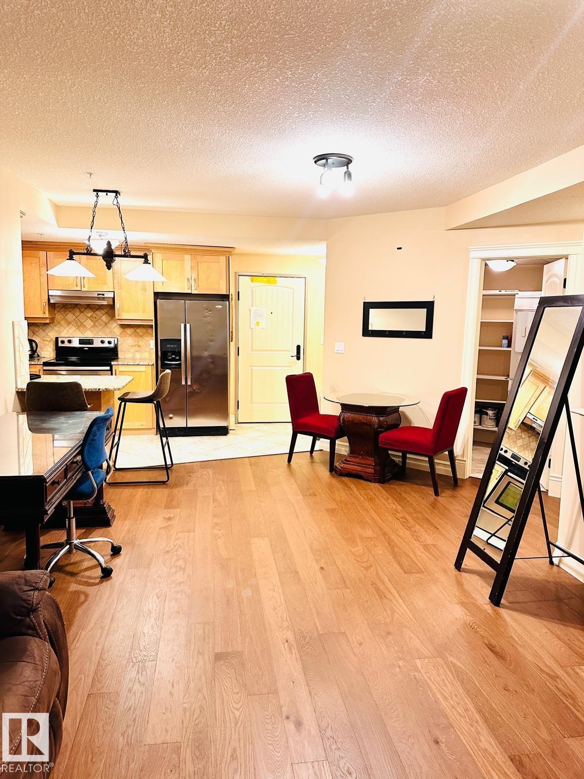Wood-finish flooring throughout, stainless steel refrigerator, light wood cabinetry, tiled kitchen backsplash, and built-in shelving - #207 10142 111 St Nw, Edmonton, AB - Indoor