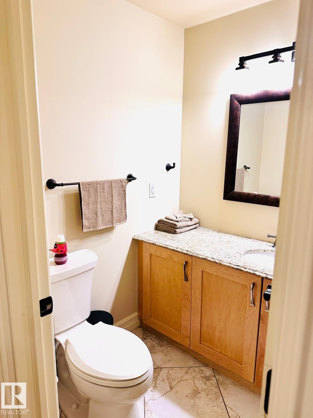 Vanity with a granite-style countertop, wood-finish cabinetry, and a framed mirror - #207 10142 111 St Nw, Edmonton, AB - Indoor Photo Showing Bathroom