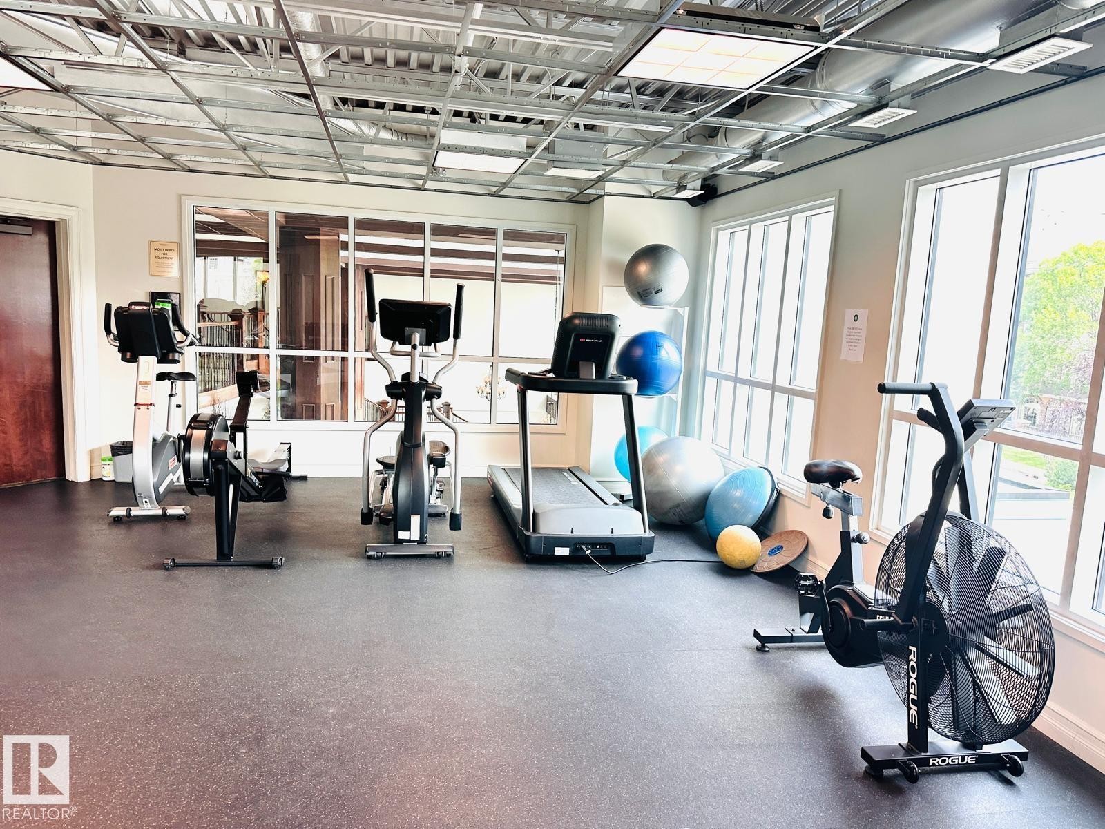 Fitness room with extensive window banks, exposed ceiling grid, recessed lighting, and rubberized flooring - #207 10142 111 St Nw, Edmonton, AB - Indoor Photo Showing Gym Room
