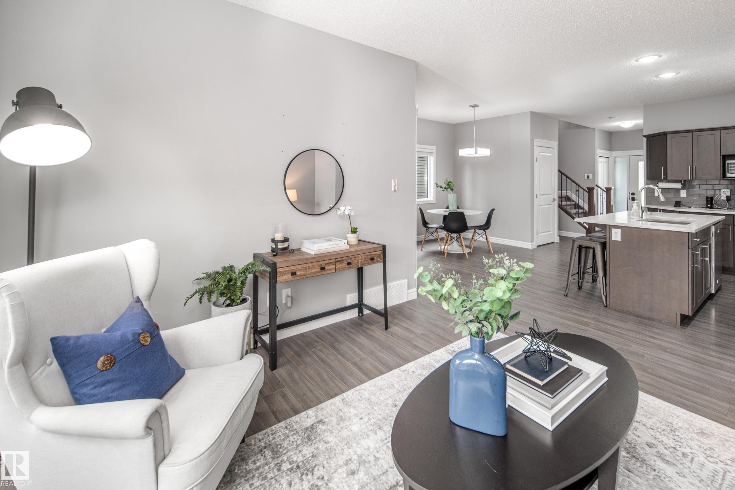 Open-concept living space featuring wood-finish flooring, a kitchen island with seating, dark wood cabinetry, a tiled kitchen backsplash, and a dining area - 16015 11 Avenue Sw, Edmonton, AB - Indoor