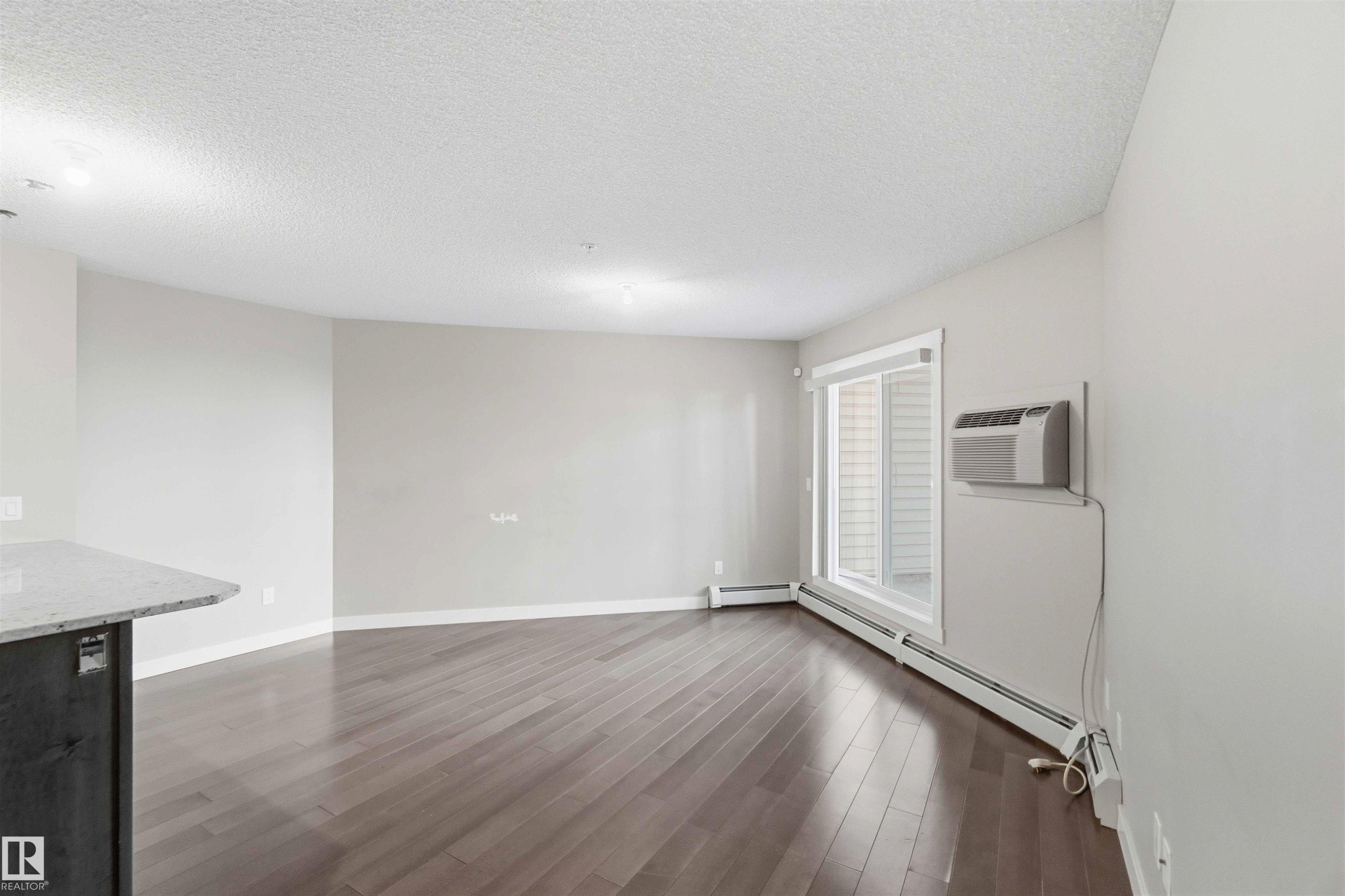 Spacious room featuring wood-finish flooring, light grey wall paint, and a textured white ceiling - #114 2207 44 Av Nw, Edmonton, AB - Indoor Photo Showing Other Room