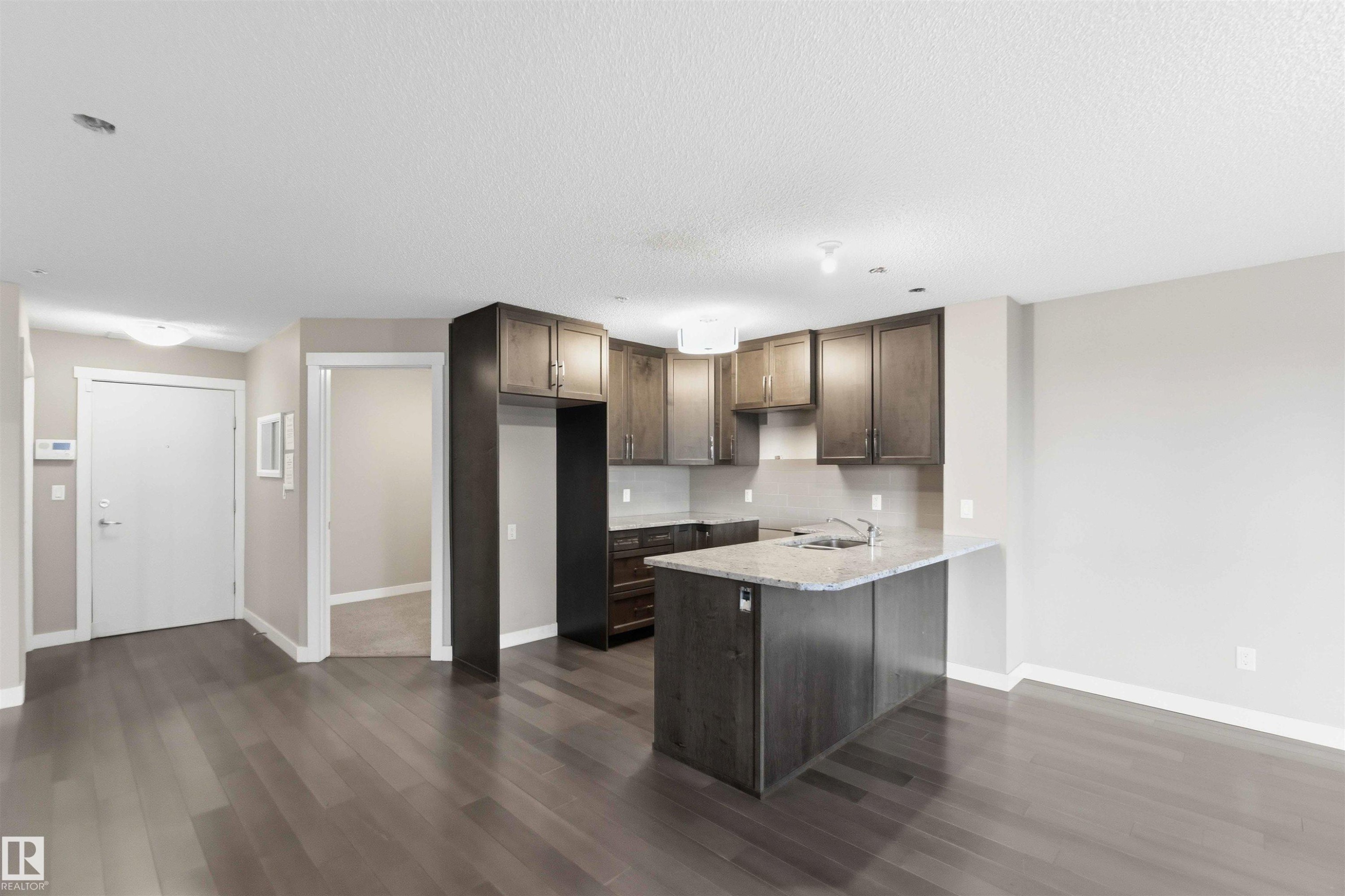 Kitchen featuring dark wood-finish cabinetry, granite countertops, and a stainless steel sink - #114 2207 44 Av Nw, Edmonton, AB - Indoor Photo Showing Kitchen