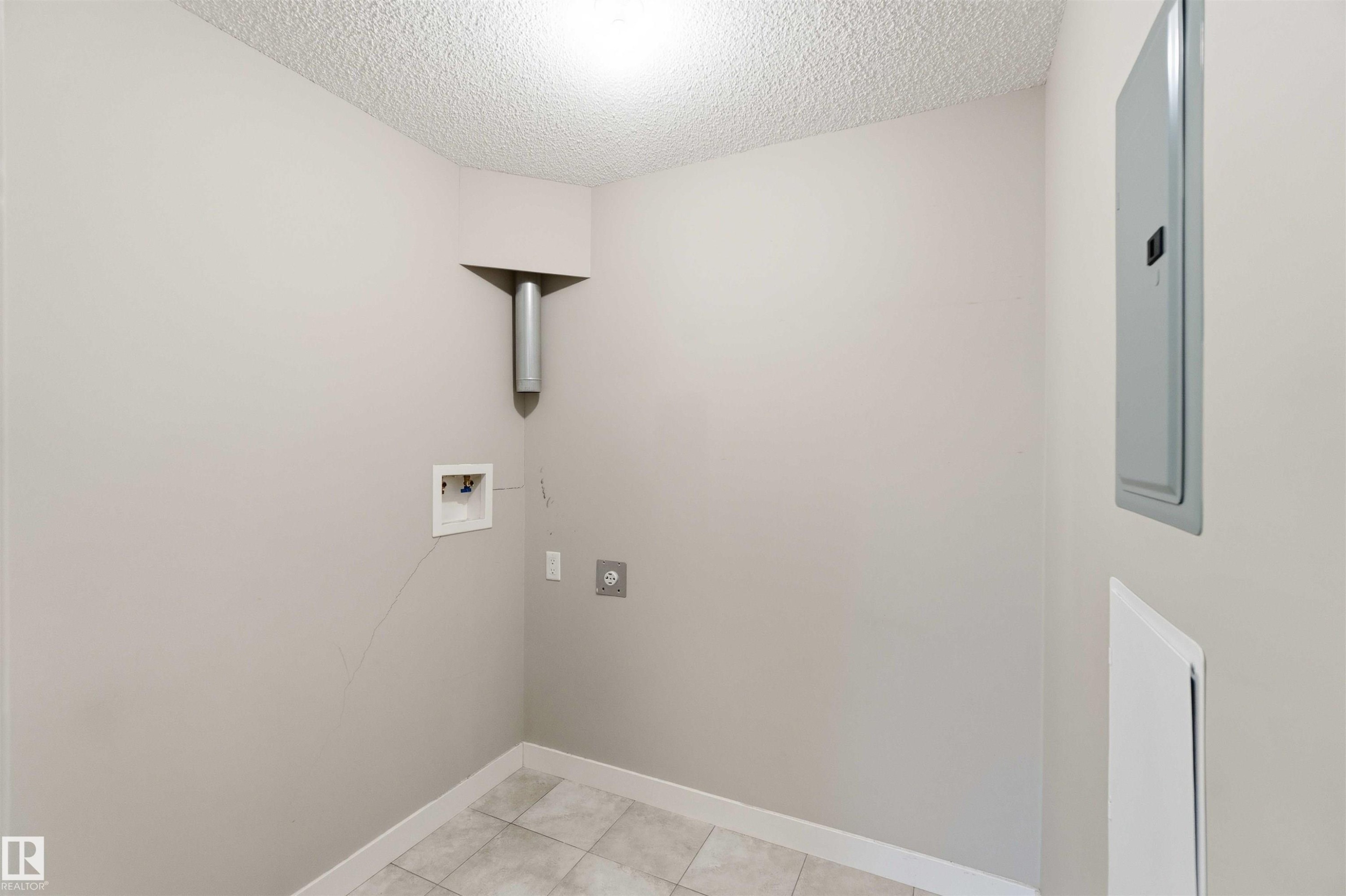 Dedicated utility space featuring light neutral wall paint, a textured ceiling, and large format square floor tiles - #114 2207 44 Av Nw, Edmonton, AB - Indoor Photo Showing Other Room