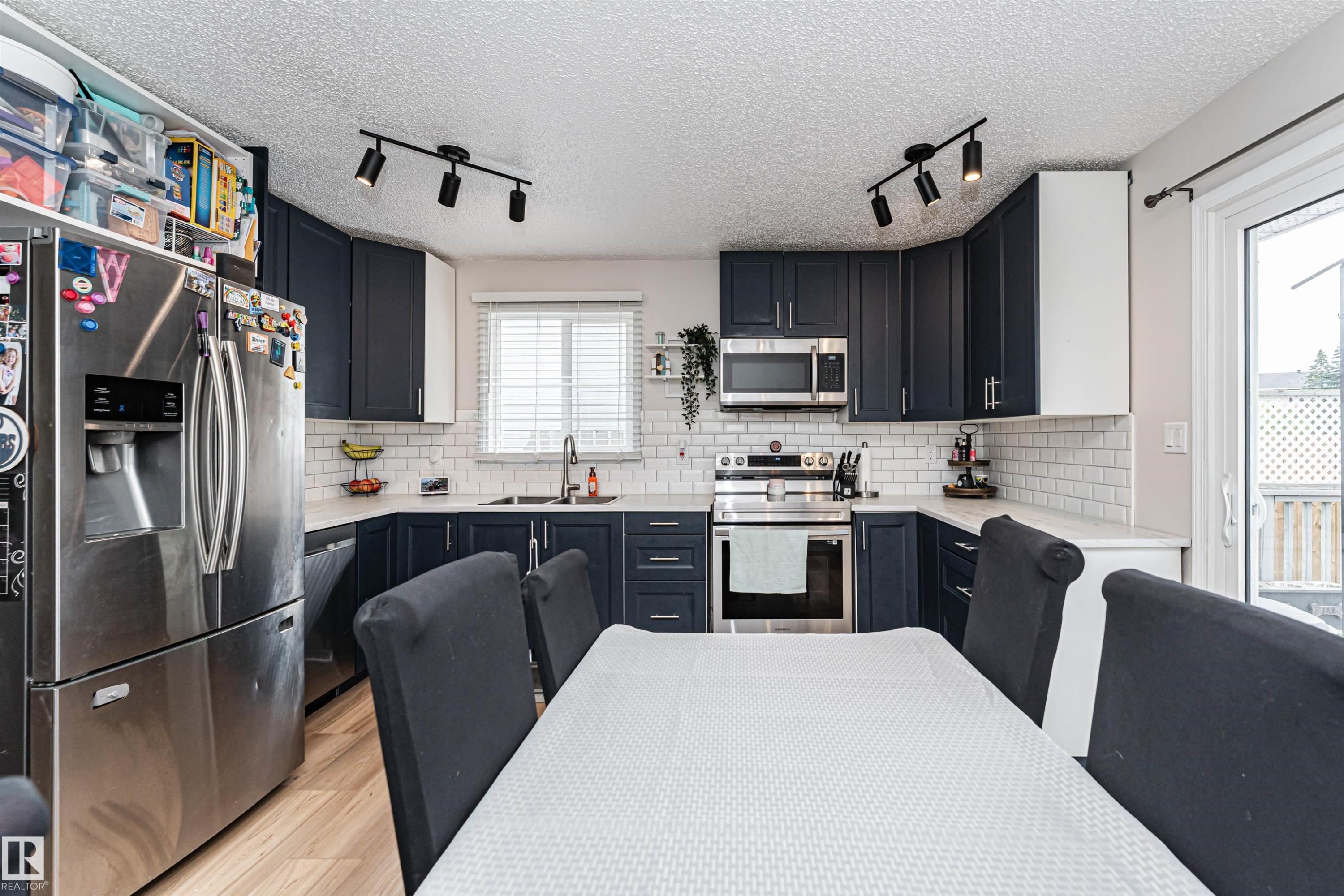 Modern kitchen featuring dark cabinetry, stainless steel appliances, light countertops, subway tile backsplash, and wood-finish flooring - 4521 29 Avenue Nw, Edmonton, AB - Indoor Photo Showing Kitchen With Double Sink With Upgraded Kitchen