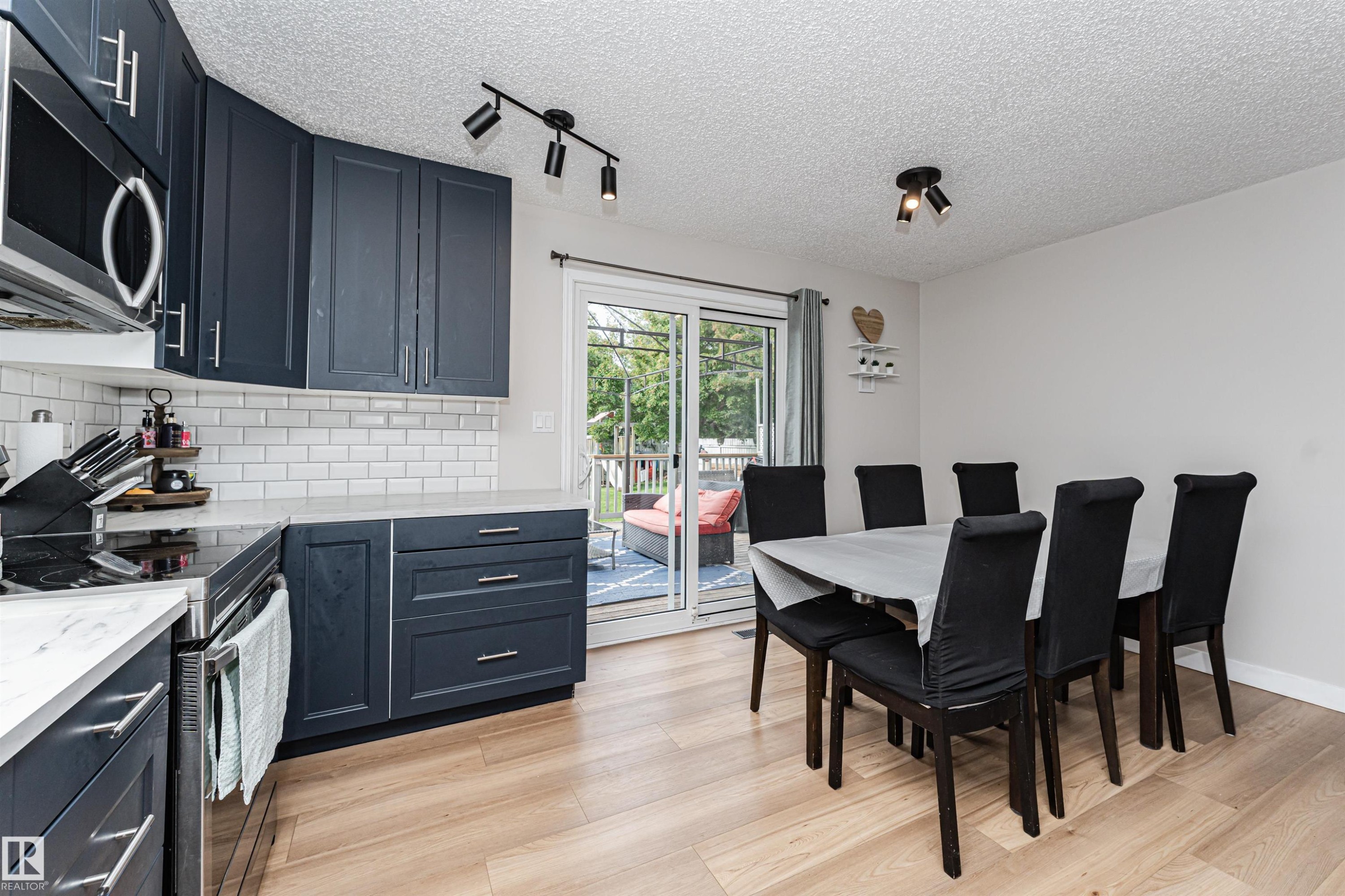 Modern kitchen with dark cabinetry, stainless steel appliances, light countertops, and a white subway tile backsplash - 4521 29 Avenue Nw, Edmonton, AB - Indoor