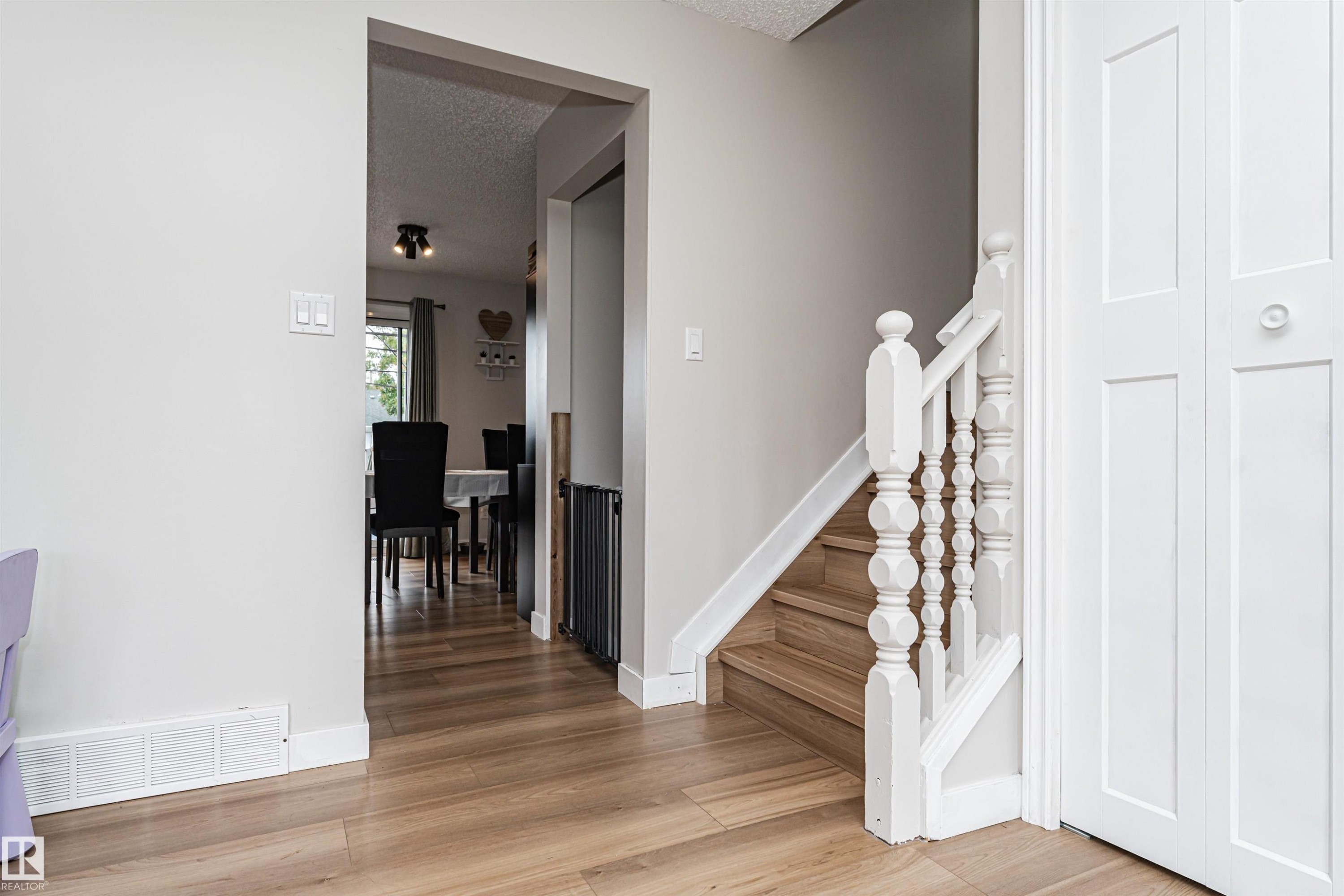 Wood-finish flooring throughout, white painted walls, white spindle staircase, and white bi-fold doors - 4521 29 Avenue Nw, Edmonton, AB - Indoor Photo Showing Other Room
