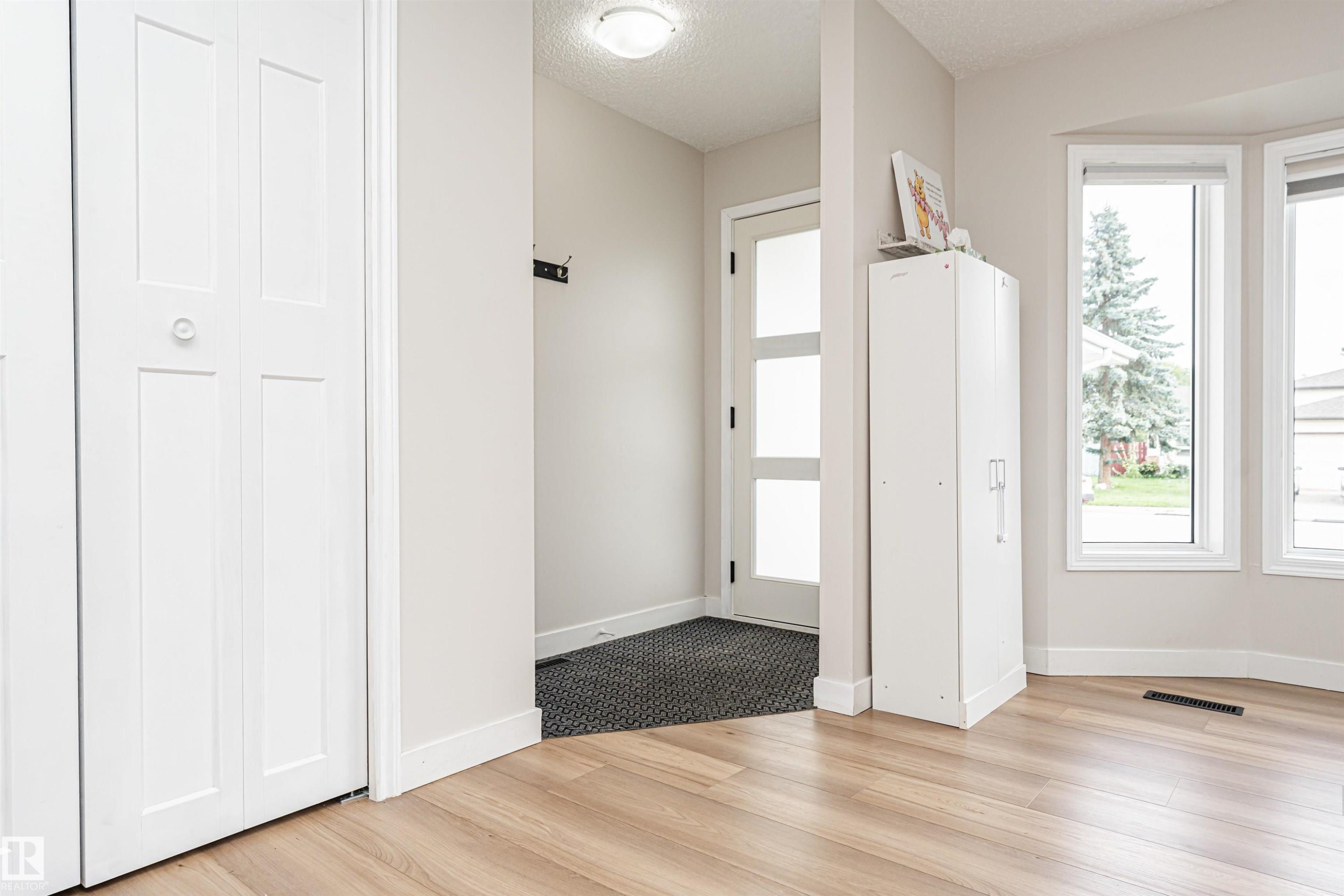 Wood-finish flooring, white bi-fold closet doors, contemporary front entry door with frosted glass panels, and multiple large windows - 4521 29 Avenue Nw, Edmonton, AB - Indoor Photo Showing Other Room