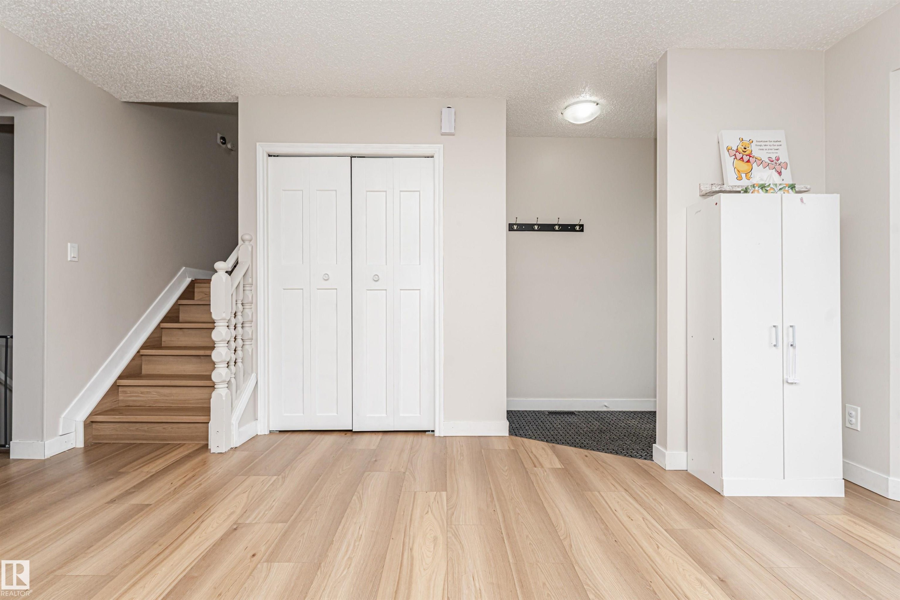 Wood-finish flooring throughout, white bi-fold doors, wood staircase with white balusters, overhead flush-mount lighting, and light-toned walls - 4521 29 Avenue Nw, Edmonton, AB - Indoor Photo Showing Other Room