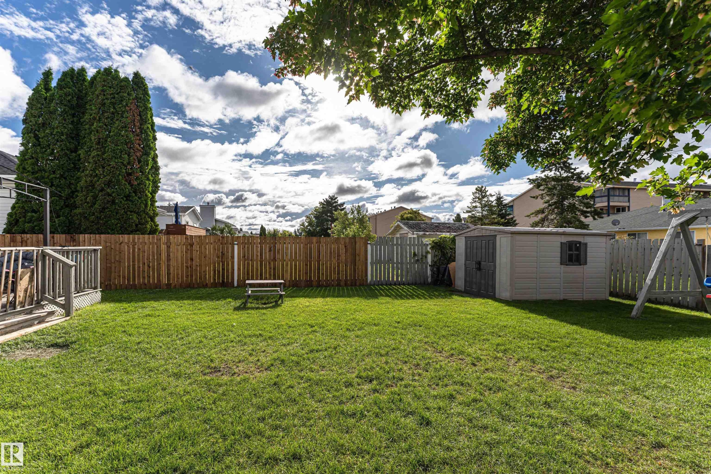 Expansive green lawn with a wood privacy fence, featuring a raised wood deck, a storage shed, and mature trees - 4521 29 Avenue Nw, Edmonton, AB - Outdoor