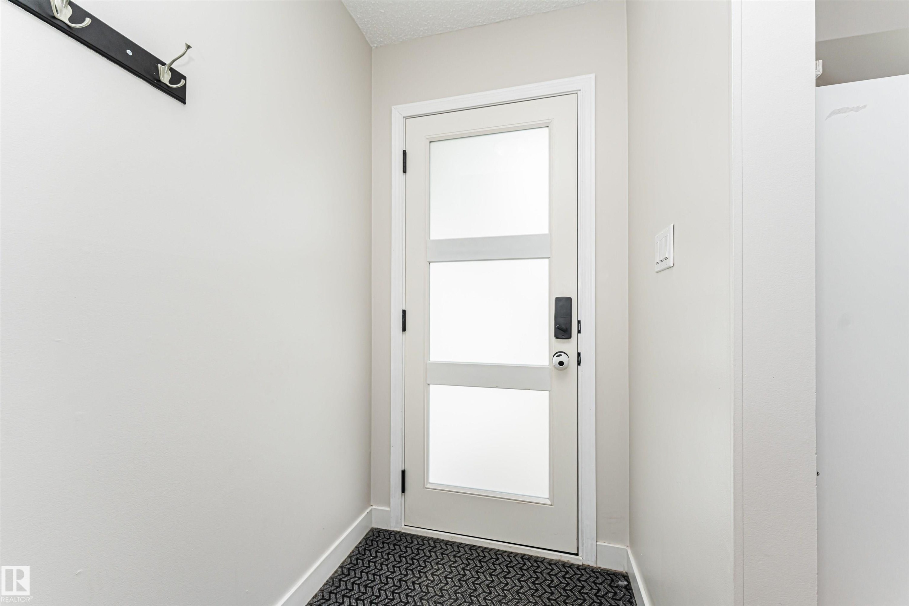 Entry door with frosted glass panels, black hardware, and a black coat rack - 4521 29 Avenue Nw, Edmonton, AB - Indoor Photo Showing Other Room
