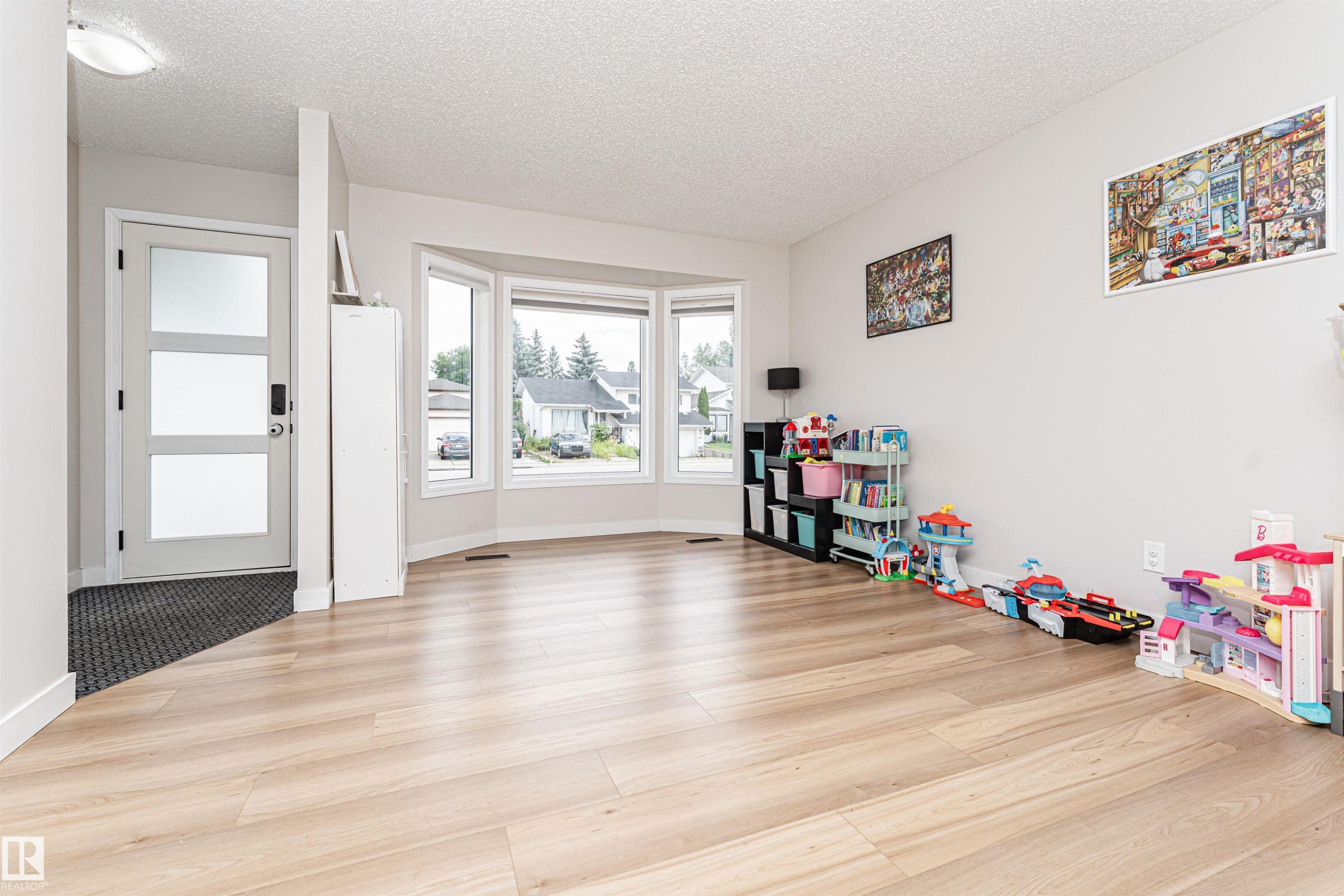 Light wood-finish flooring, bay window with multiple panes, contemporary entry door with frosted panels, and recessed ceiling lighting - 4521 29 Avenue Nw, Edmonton, AB - Indoor Photo Showing Other Room