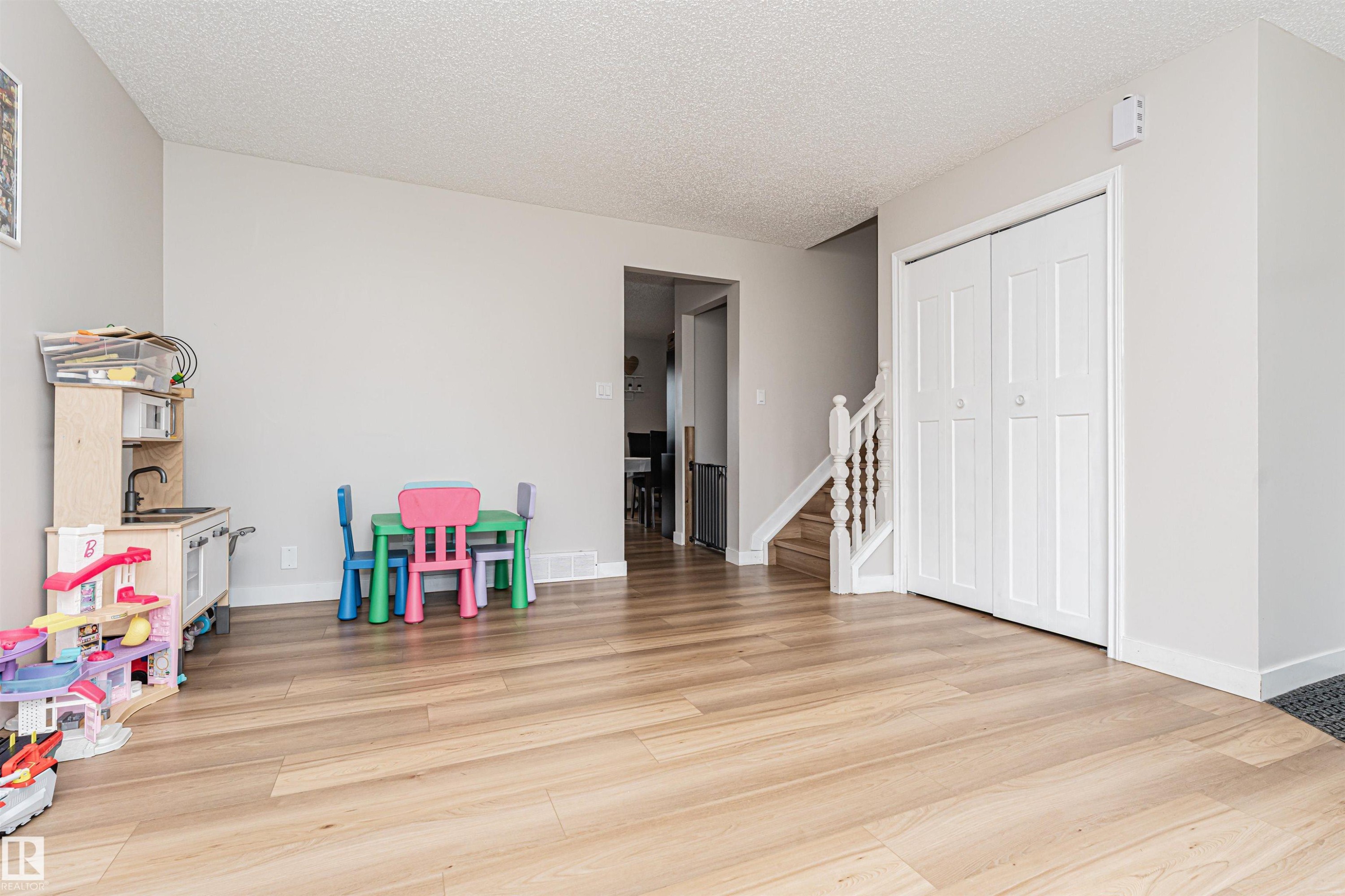 Wood-finish flooring, light gray wall tones, white baseboards, bi-fold closet doors, and a wood staircase with white balusters - 4521 29 Avenue Nw, Edmonton, AB - Indoor Photo Showing Other Room