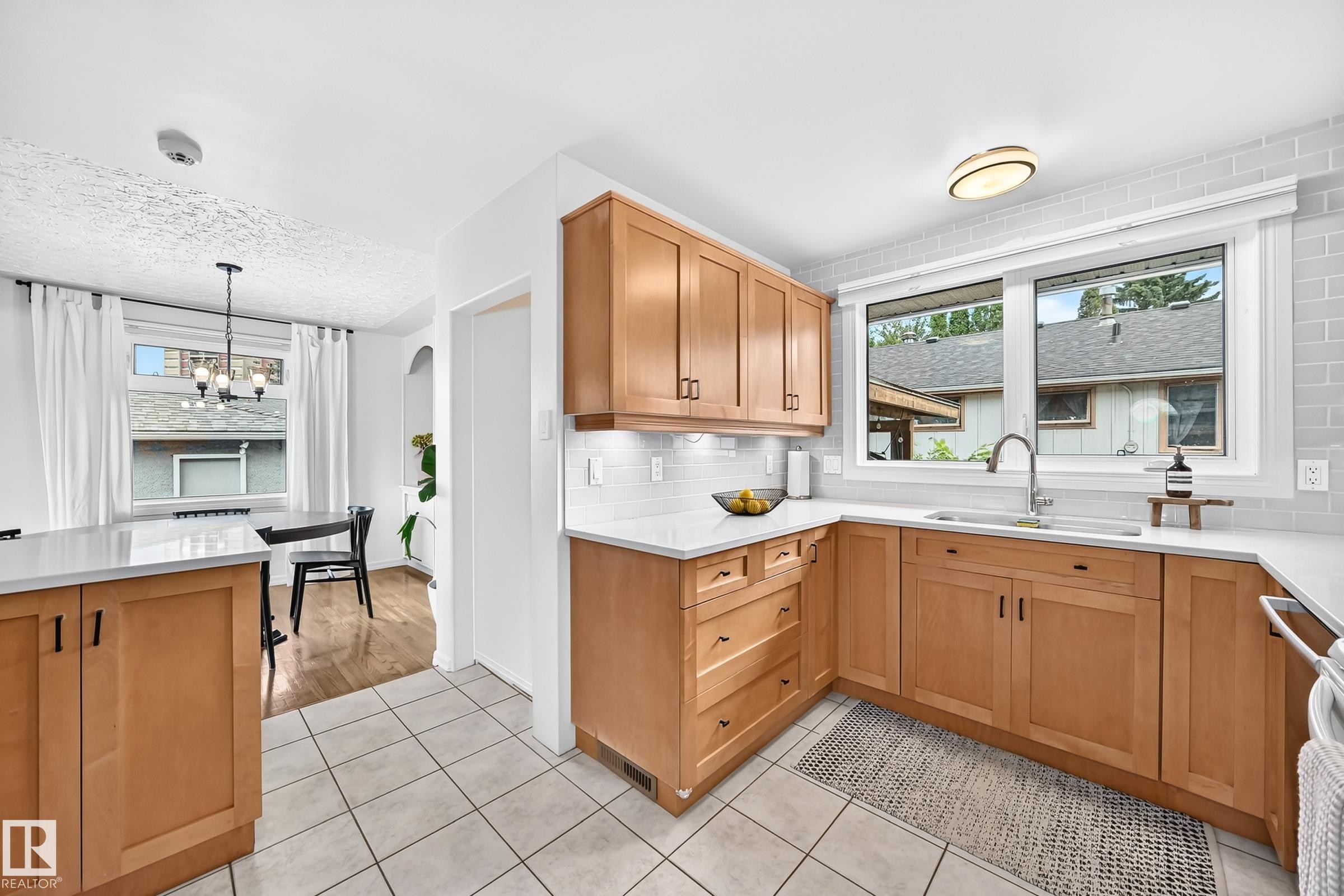 Light wood-finish cabinetry with dark hardware, L-shaped countertop, undermount sink with gooseneck faucet, light tile backsplash, and light tile flooring - 16406 87A Avenue Nw, Edmonton, AB - Indoor Photo Showing Kitchen