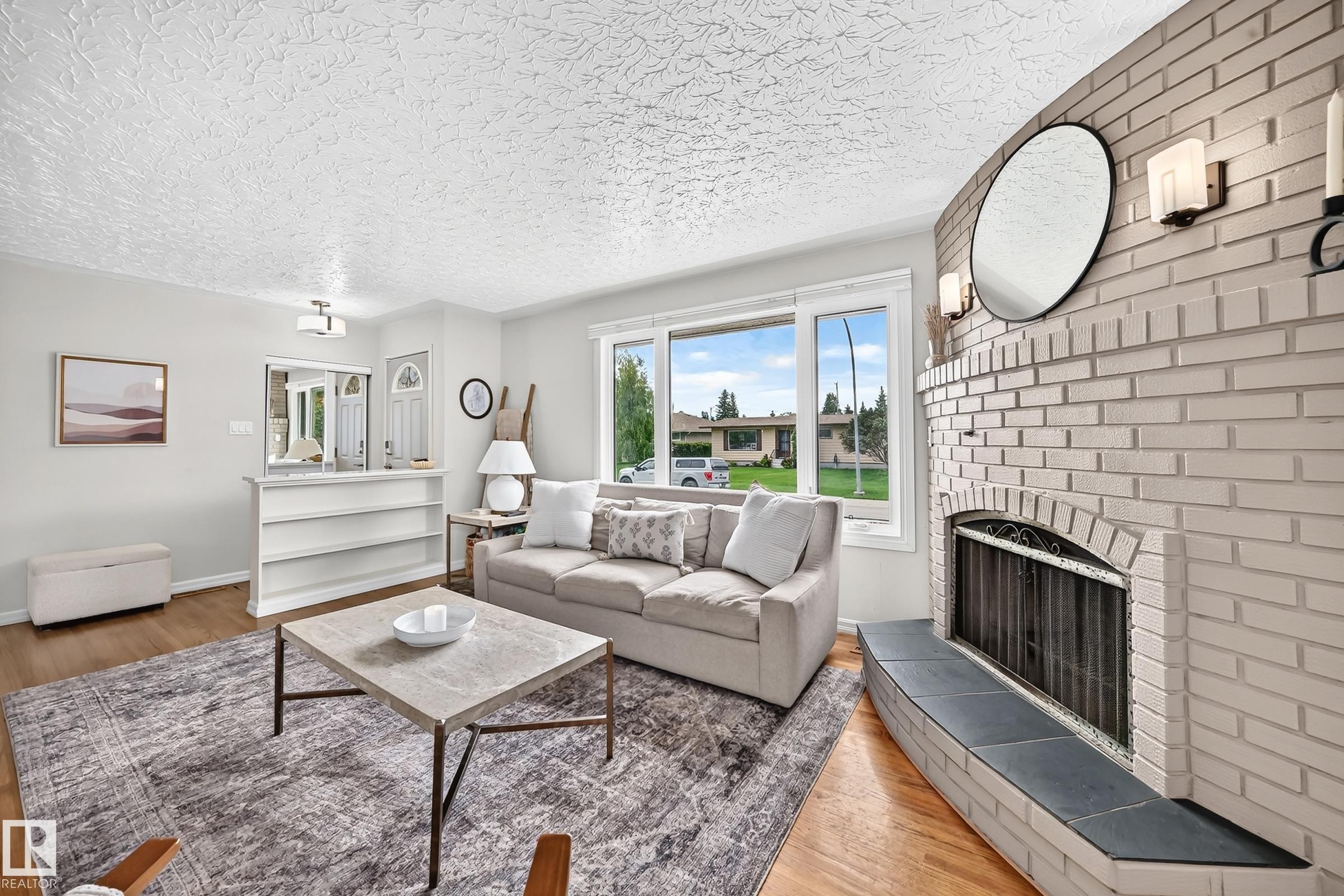 Wood-finish flooring throughout, complemented by a painted brick fireplace with a hearth - 16406 87A Avenue Nw, Edmonton, AB - Indoor Photo Showing Living Room With Fireplace